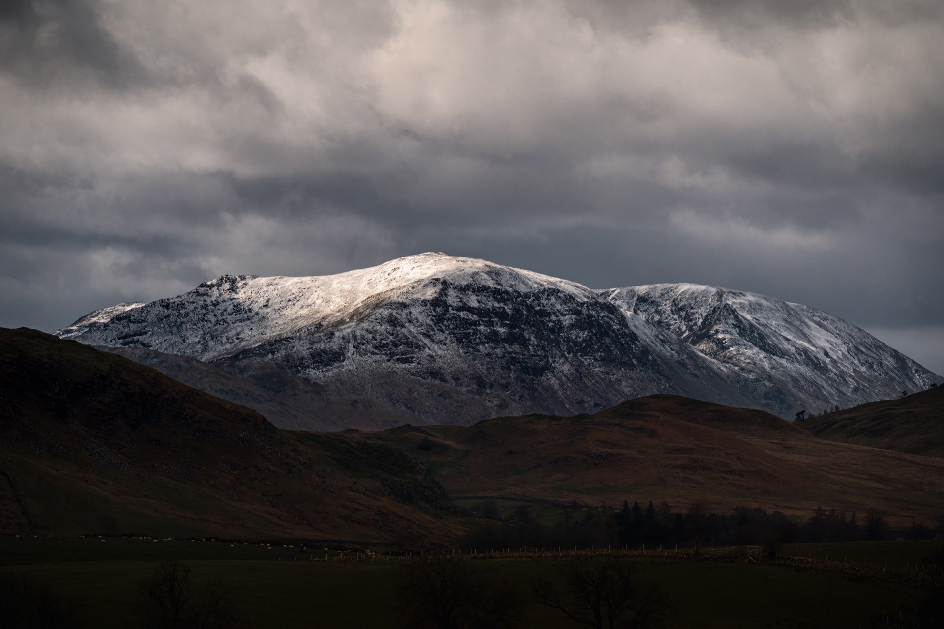 Hart Crag and Fairfield mountain range in a moody dark scene, capped with snow.