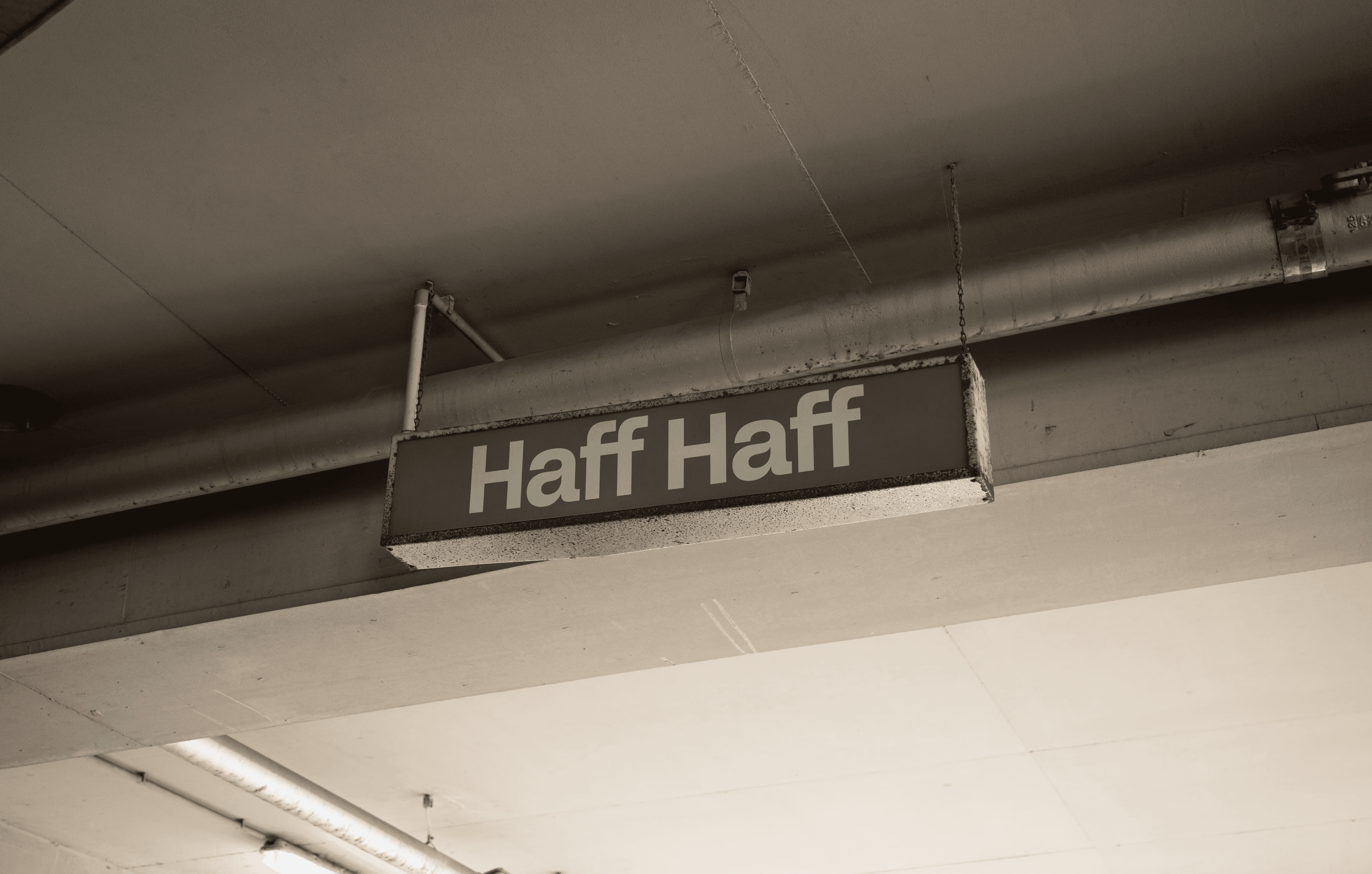 A weathered, industrial-style hanging sign with the words "Haff Haff" in a bold, sans-serif typeface. This mockup demonstrates the studio's capability in environmental graphic design and brand identity application, showing how a minimalist Swiss aesthetic can be integrated into raw, urban settings.