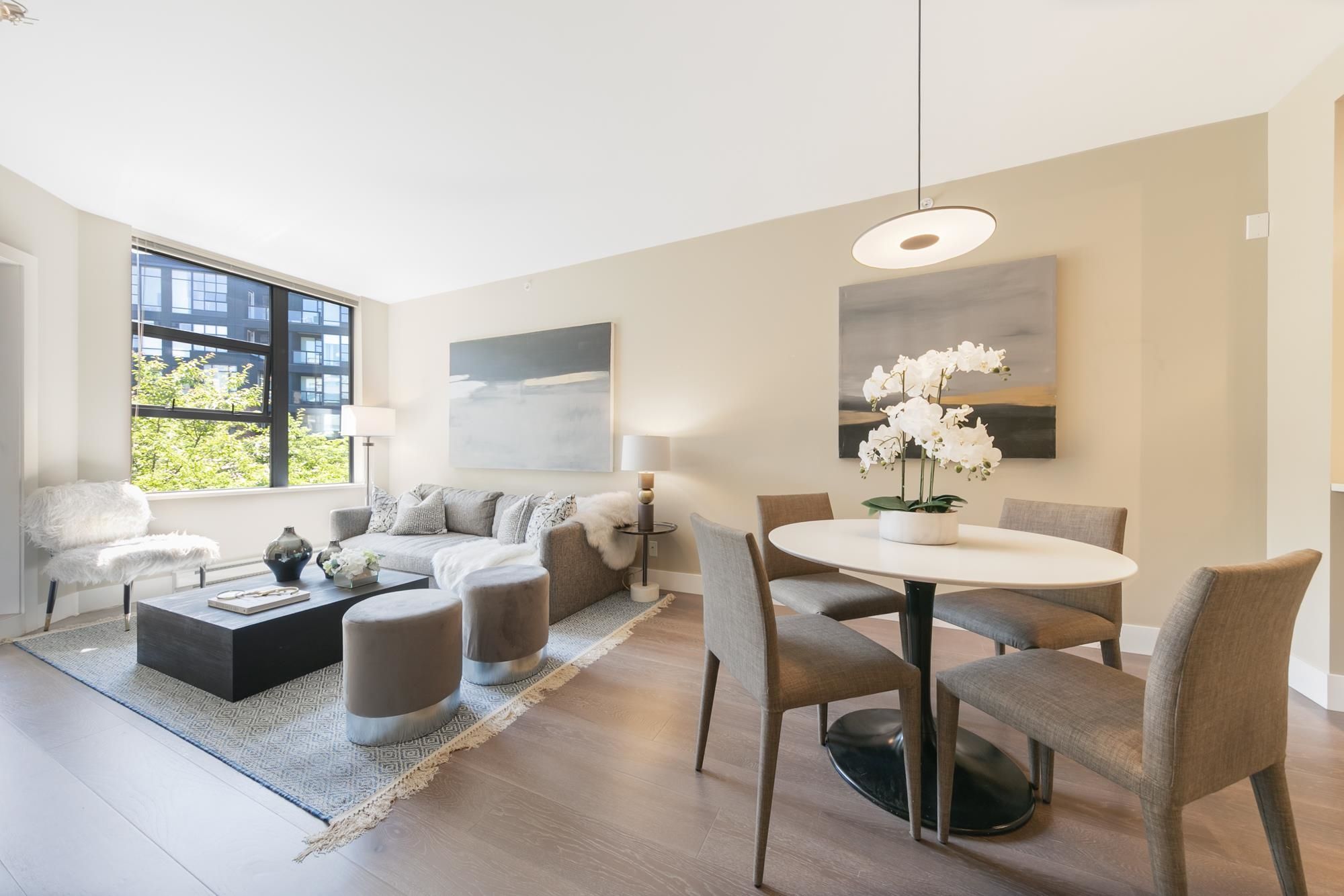 Bright, modern living room with a dining area, large windows, and stylish furniture, creating an inviting atmosphere.