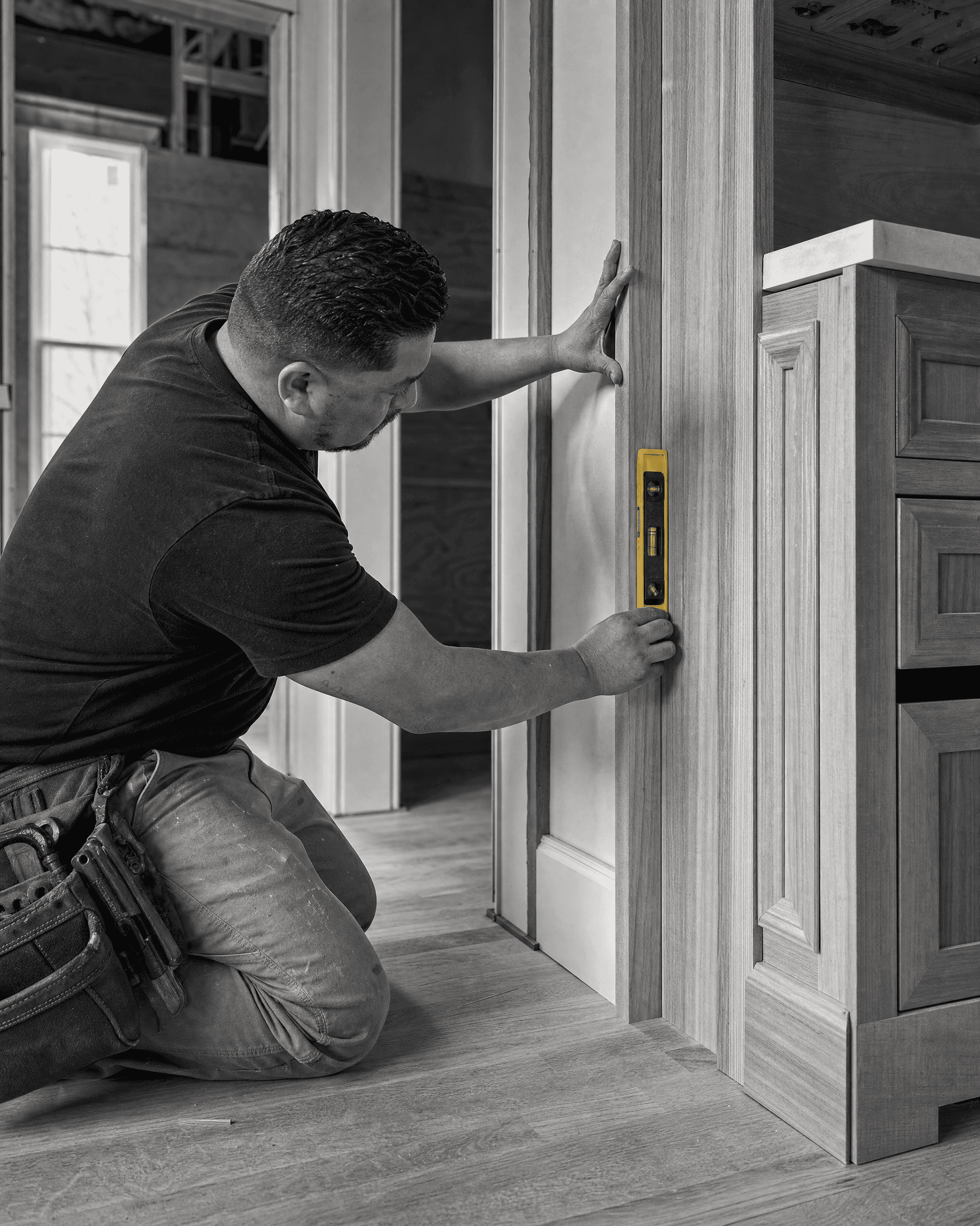 Craftsperson checking vertical alignment of custom wood millwork with a level during finish installation.