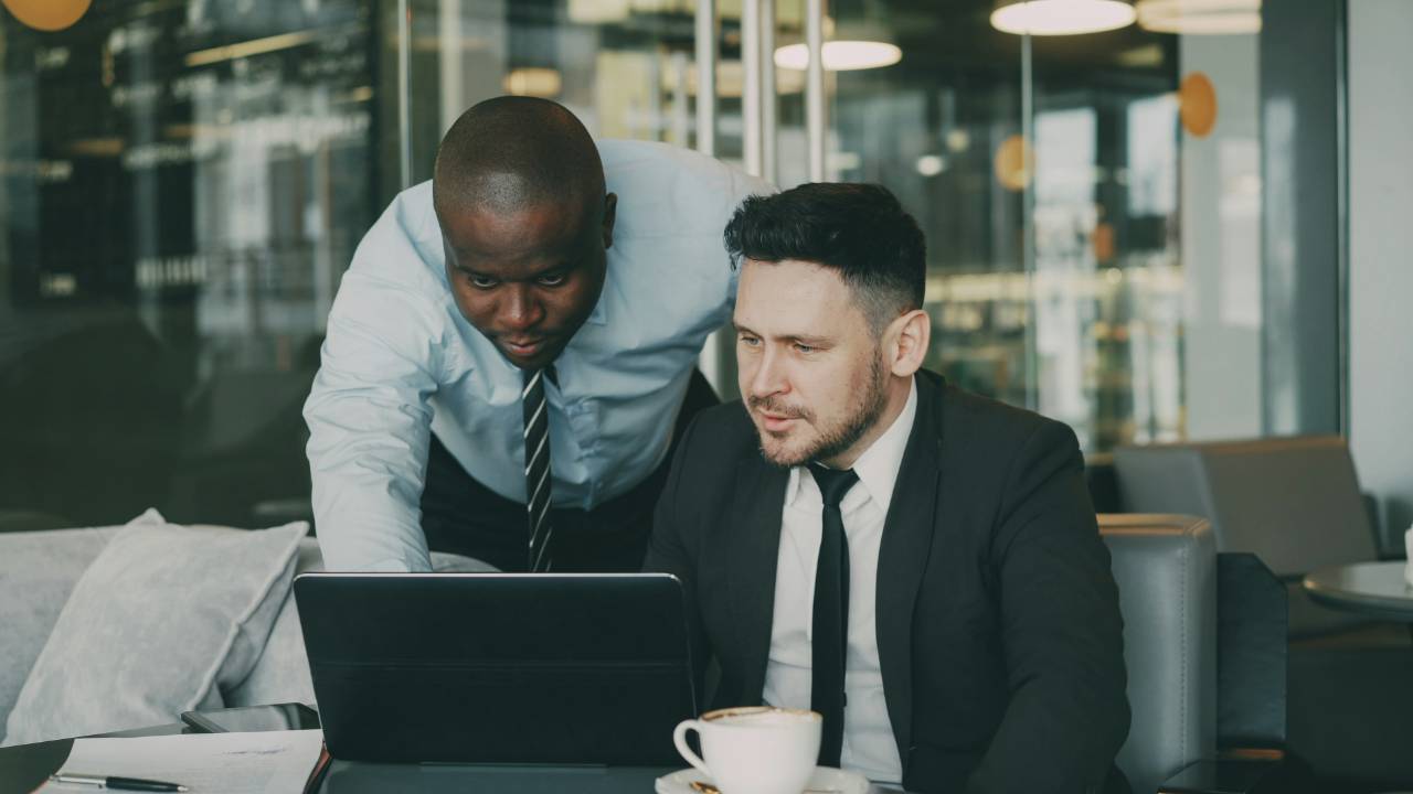 Two colleagues in business dress studying a laptop together in an office.