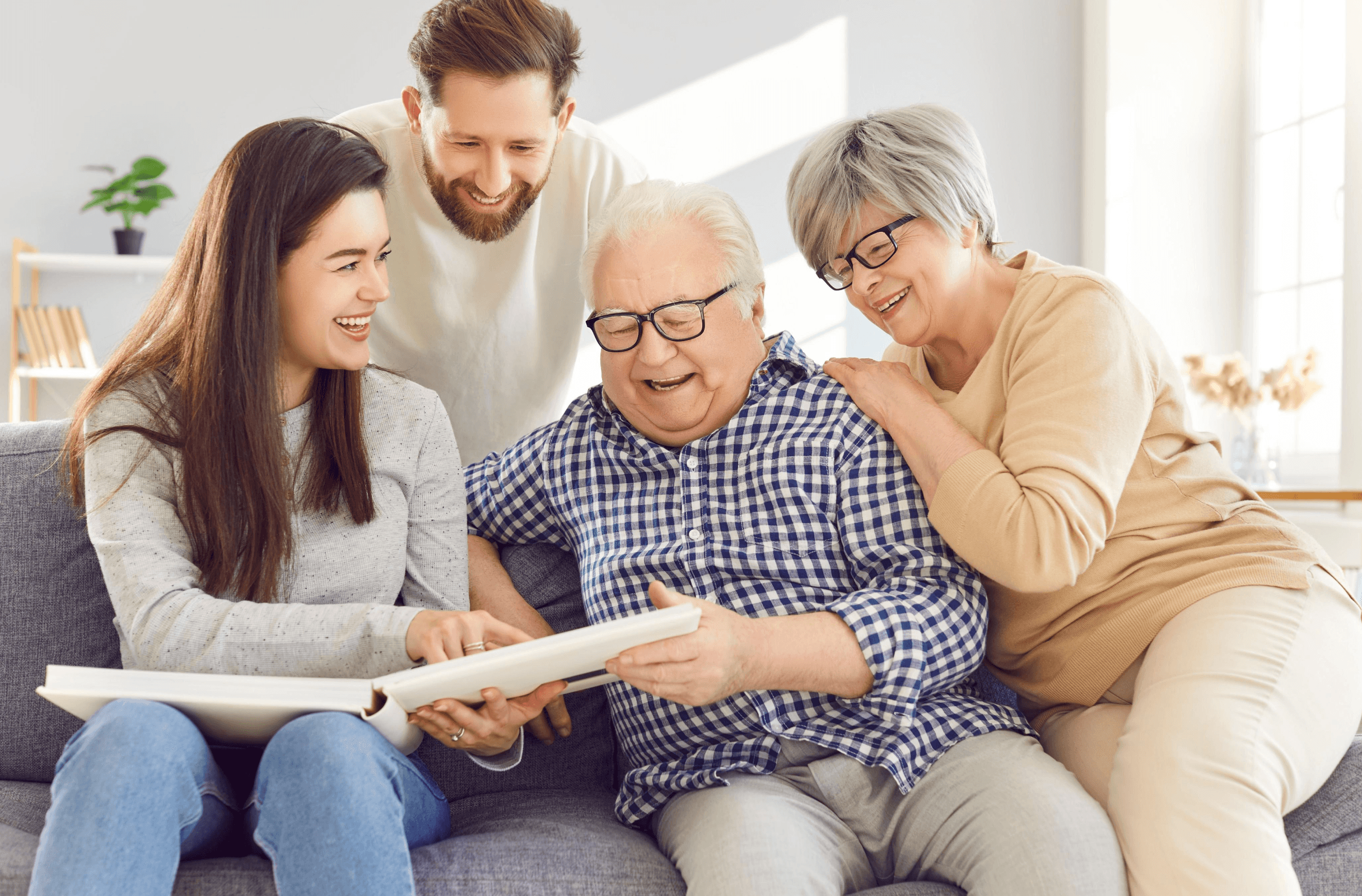 A joyful family scene showing a young couple and an elderly man and woman smiling together while looking at a book, representing family harmony and care.
