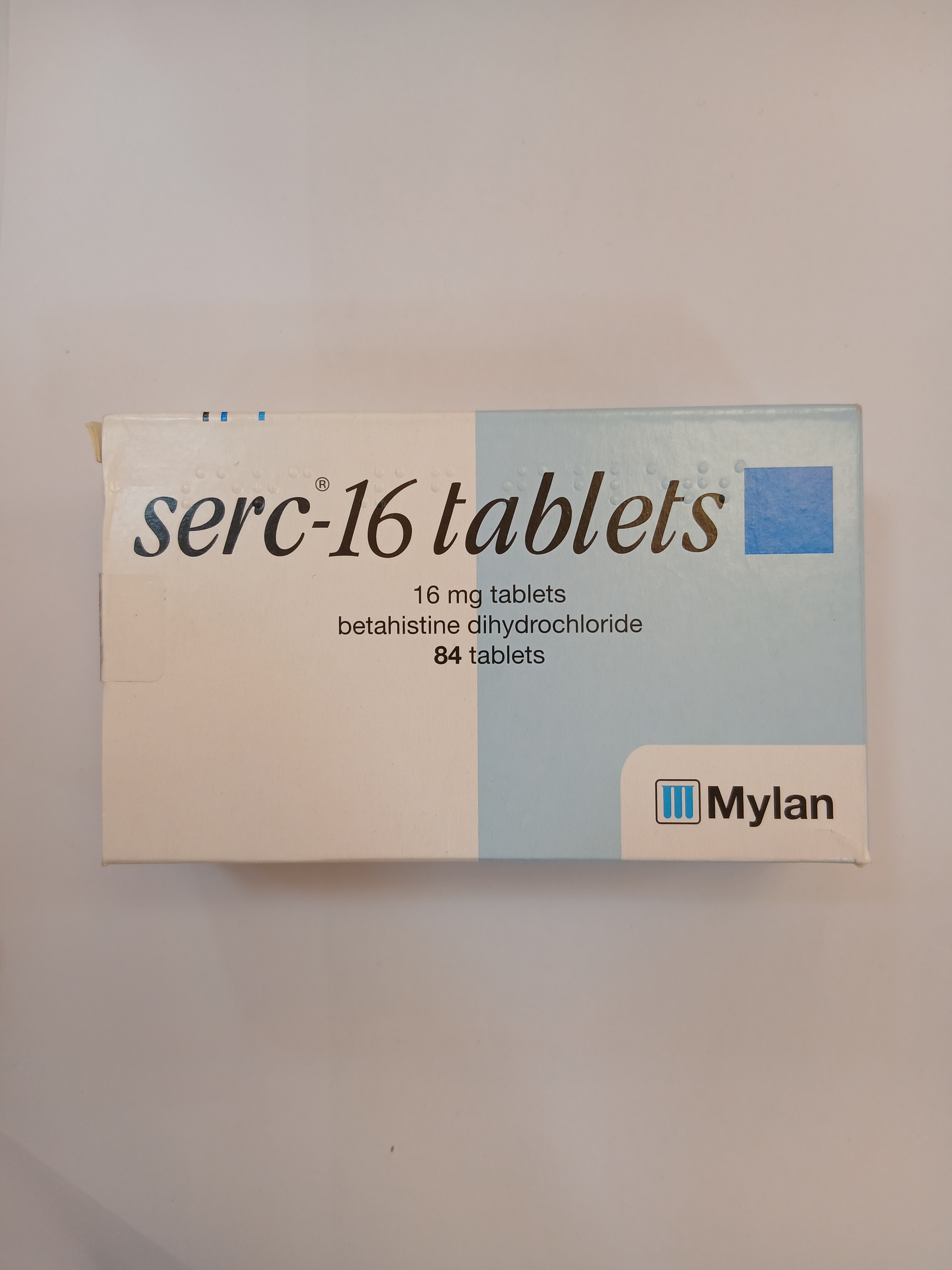 A white cardboard box packaging displays printed text indicating it contains 84 light-colored tablets, with a blue section on the top right corner and the manufacturer’s logo at the bottom.