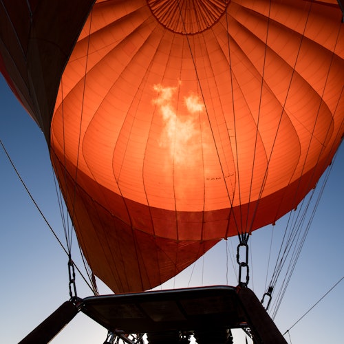 Een uitzicht van onder een luchtballon, waarin de oranje stof wordt benadrukt die door zonlicht wordt verlicht tegen een helderblauwe lucht.