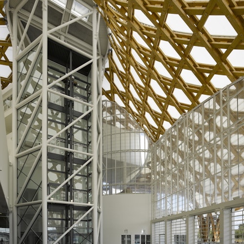 现代建筑的内部设计，配有玻璃电梯、大型玻璃墙和木质格栅天花板。