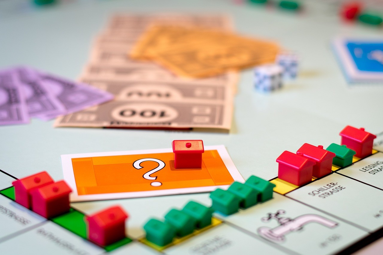 A corner of the Monopoly board game with an orange house on an orange card, surrounded by green and red houses and money.