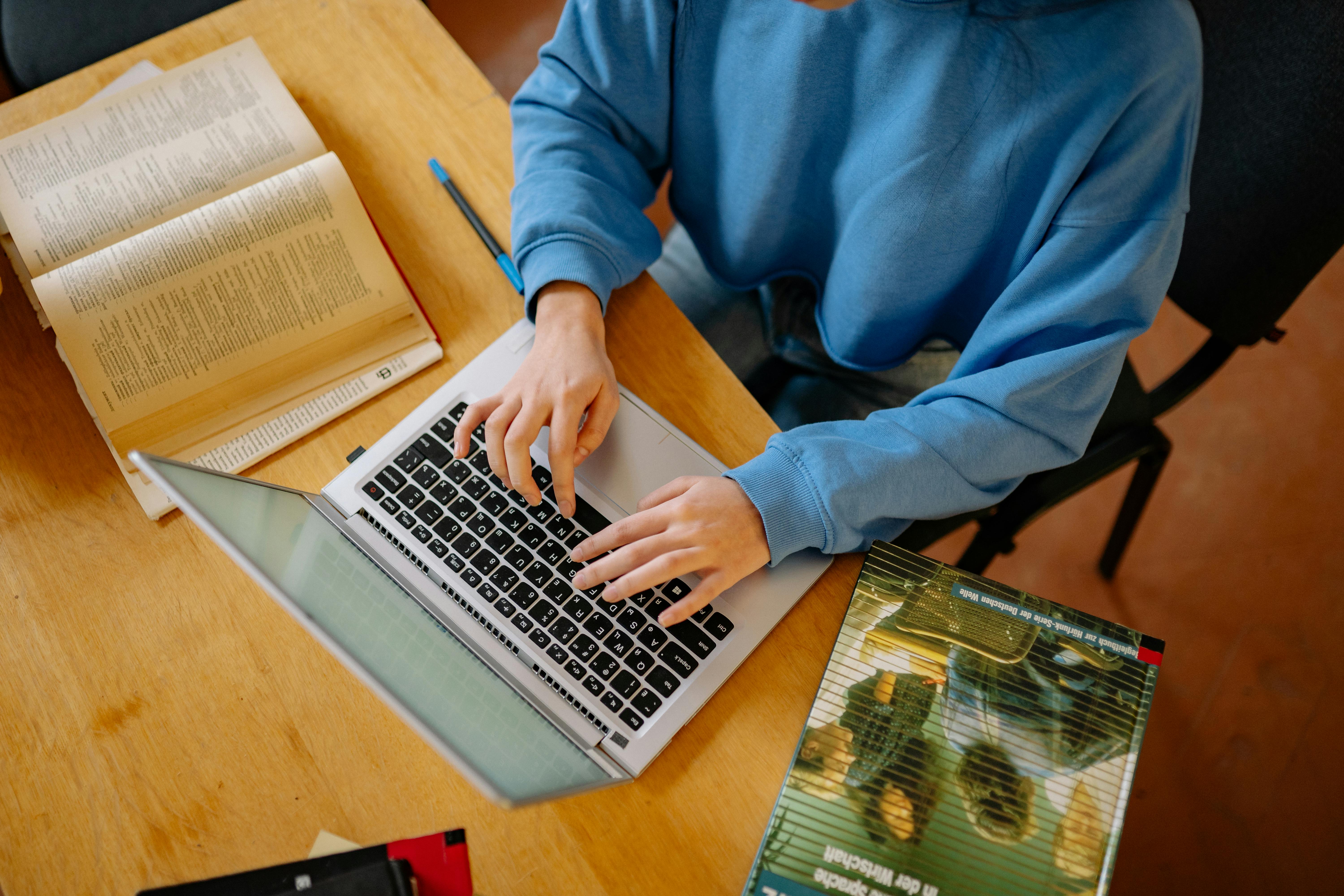 a-student-typing-on-a-laptop-surrounded-by-open-books,-focusing-on-research-and- - yan-krukau (pexels)
