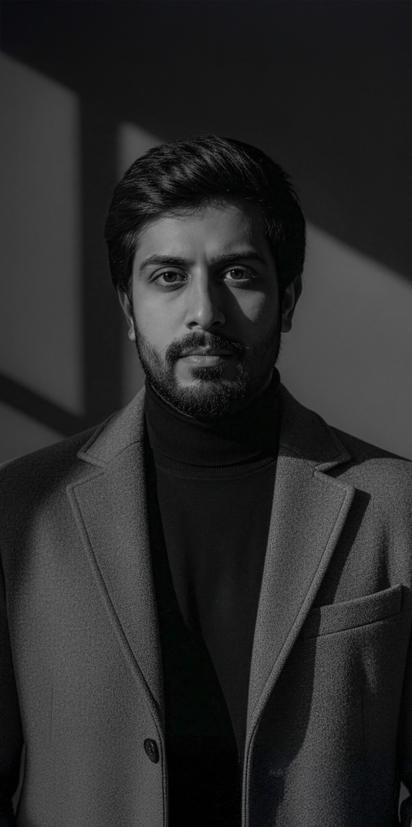 A man in a brown blazer and a woman in a light sweater sit at a desk with a laptop, discussing something. The room is dimly lit, creating a focused atmosphere.