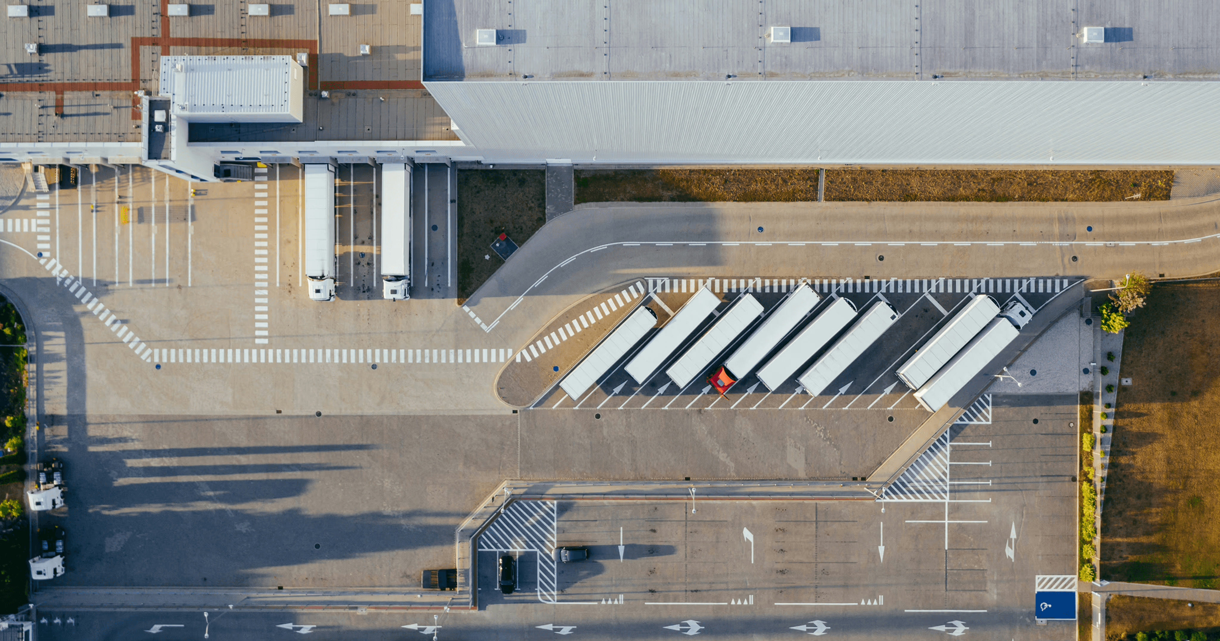 Overhead view of a freight warehouse with multiple semi-trucks staged at loading docks and parking bays.