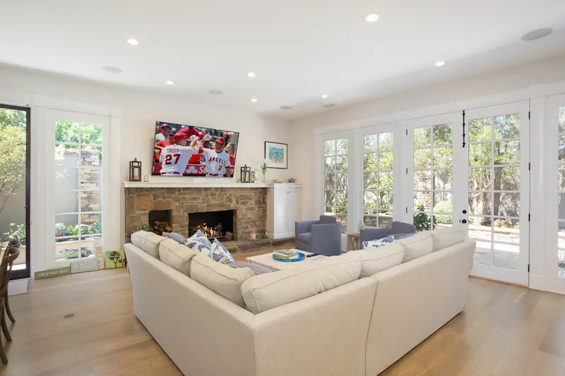 Bright and spacious living room with several french doors, white couches and stone clad fireplace from the Big Canyon Remodel project. Photo by Chris Darnall.