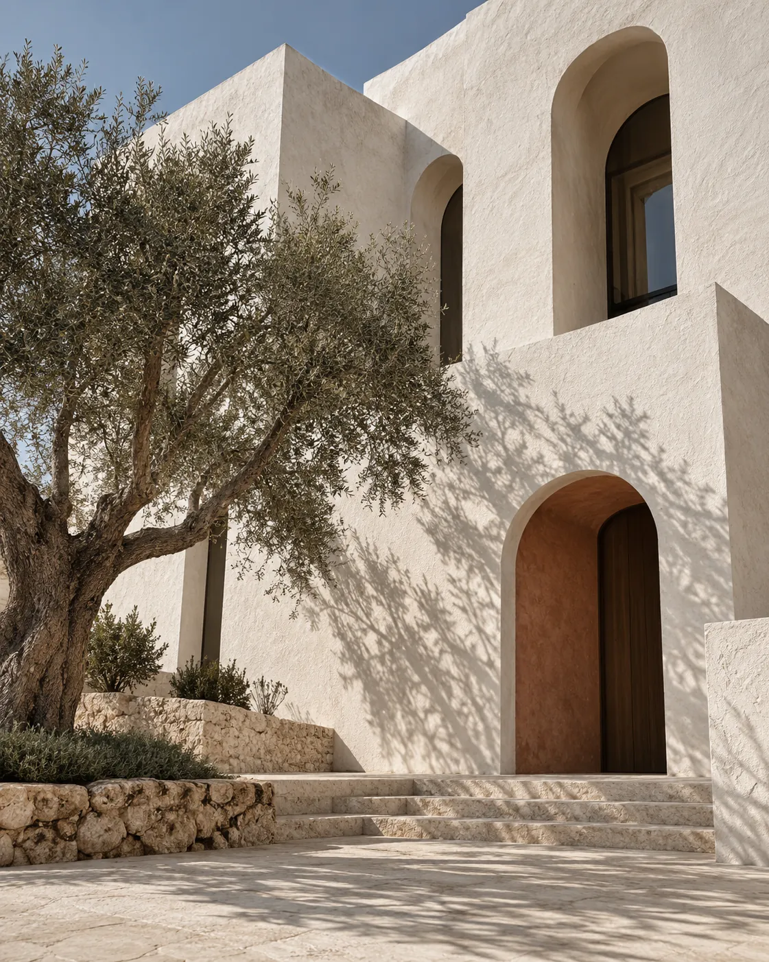 North facade of Casa Vela, whitewashed lime plaster with deep arched openings and an olive tree in front