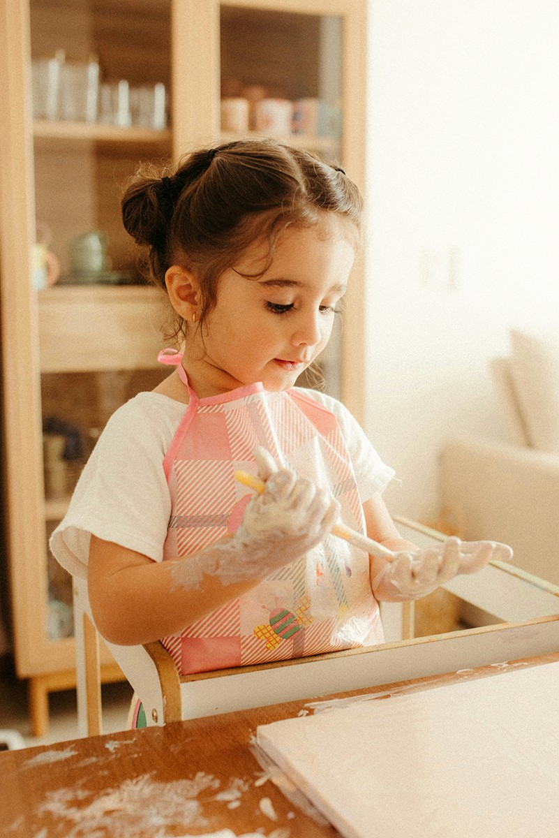 A young girl with messy hands paints at a table.