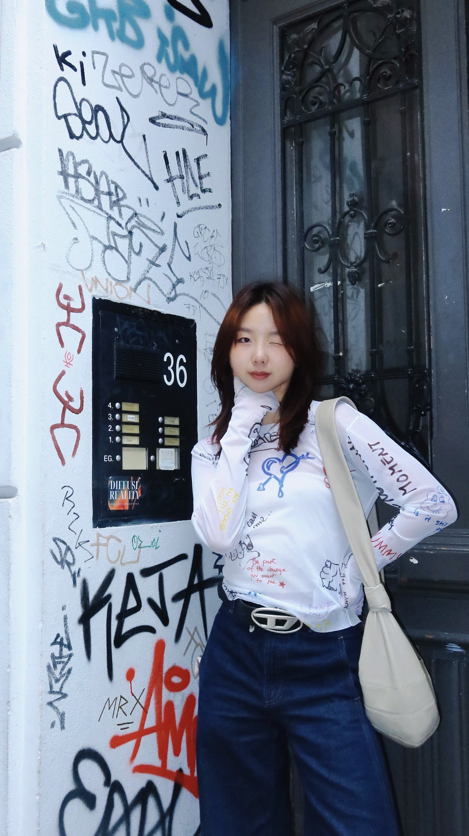 Una persona con una camiseta negra y pantalones de color claro está de pie en la cima rocosa de una montaña al atardecer, sosteniendo una cámara frente a su cara para tomar una foto. Un mar de nubes se extiende detrás de ellos, iluminado por la luz dorada del sol poniente.