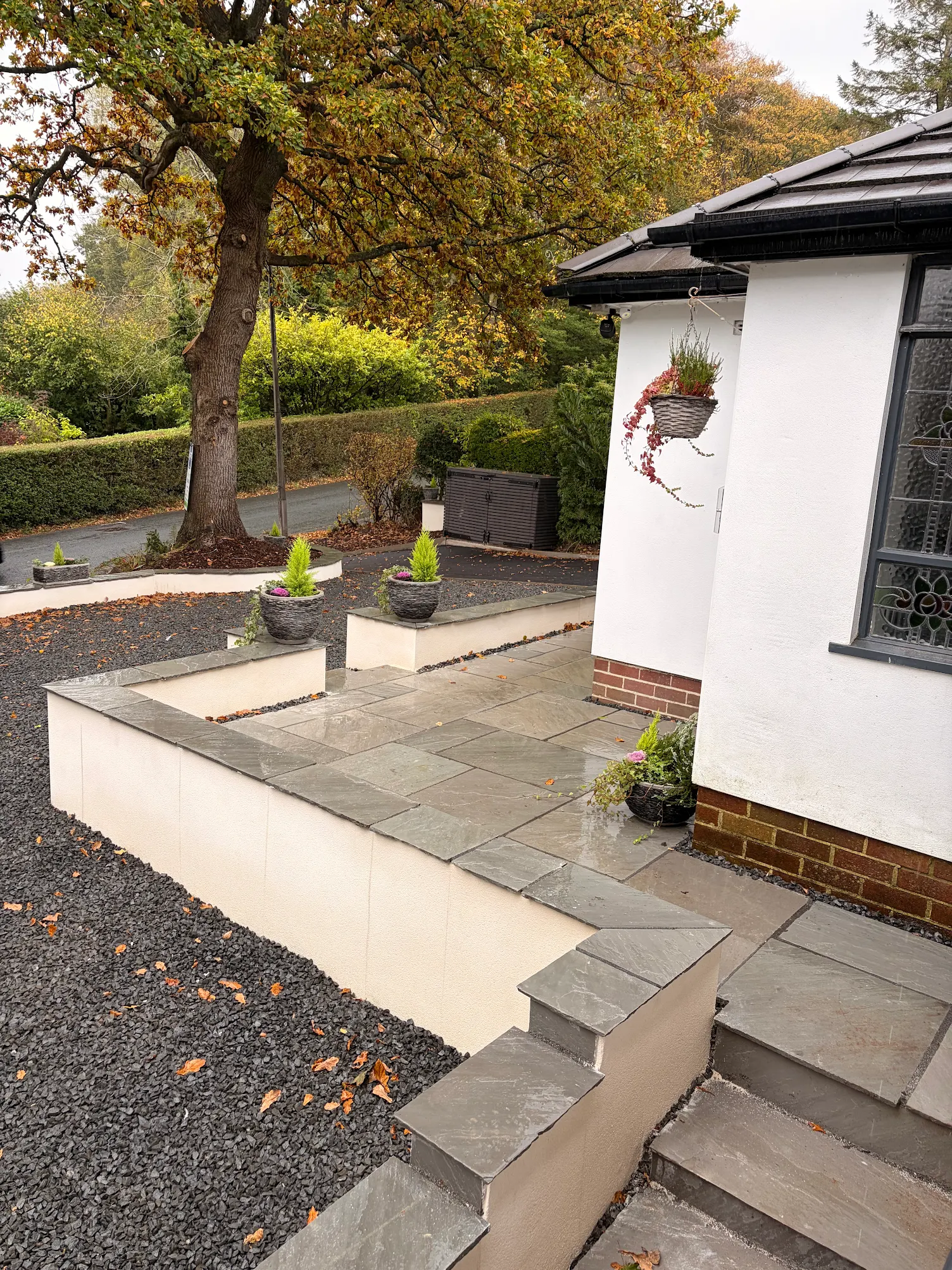 A modern patio entrance features clean, rectangular stone tiles with potted plants and a lush, leafy backdrop, enhancing the contemporary exterior design.