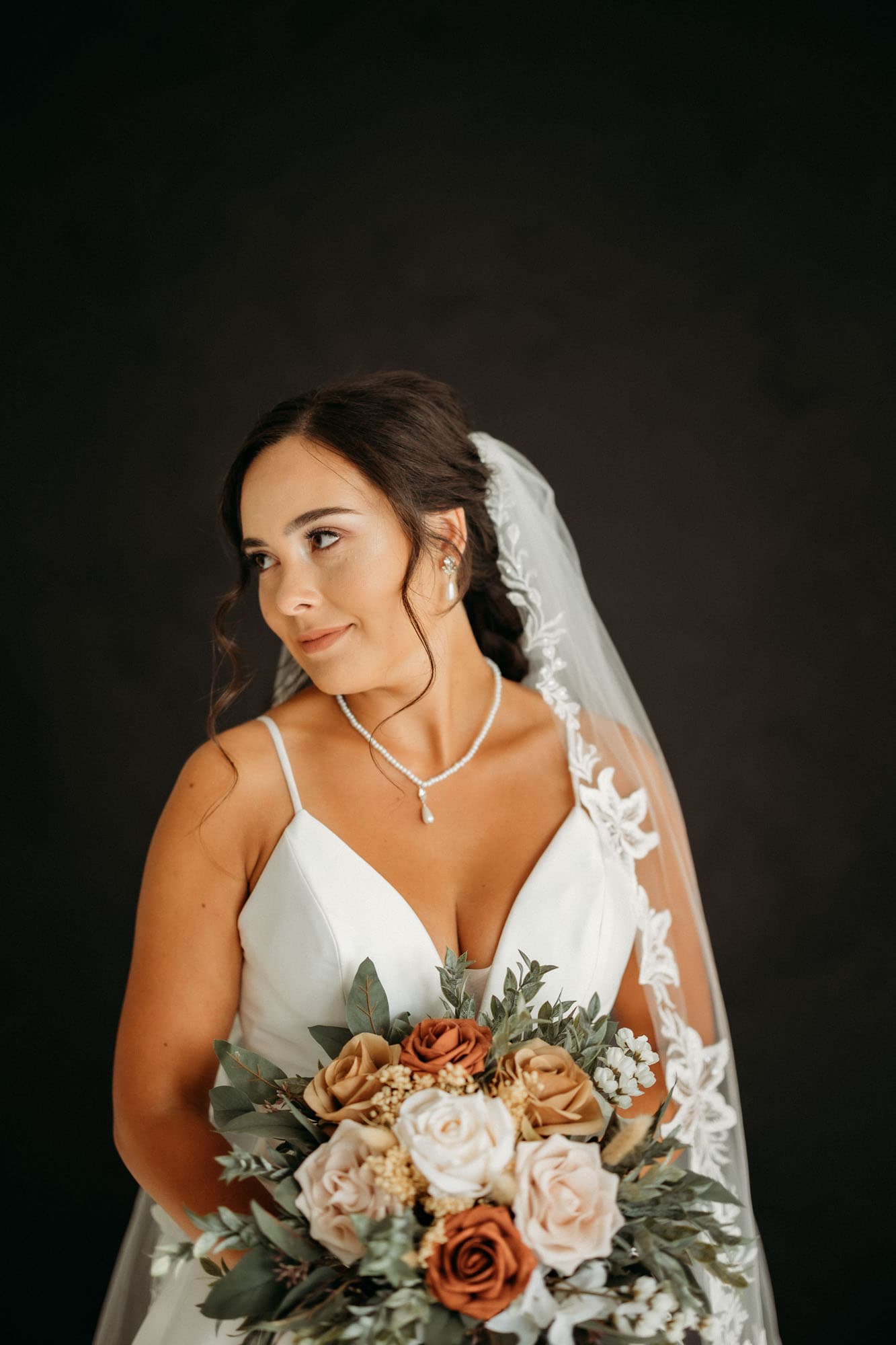 The bride looks over her shoulder, wearing a long veil with lace details, shot at Revelator Studio, a natural light studio in Shreveport.