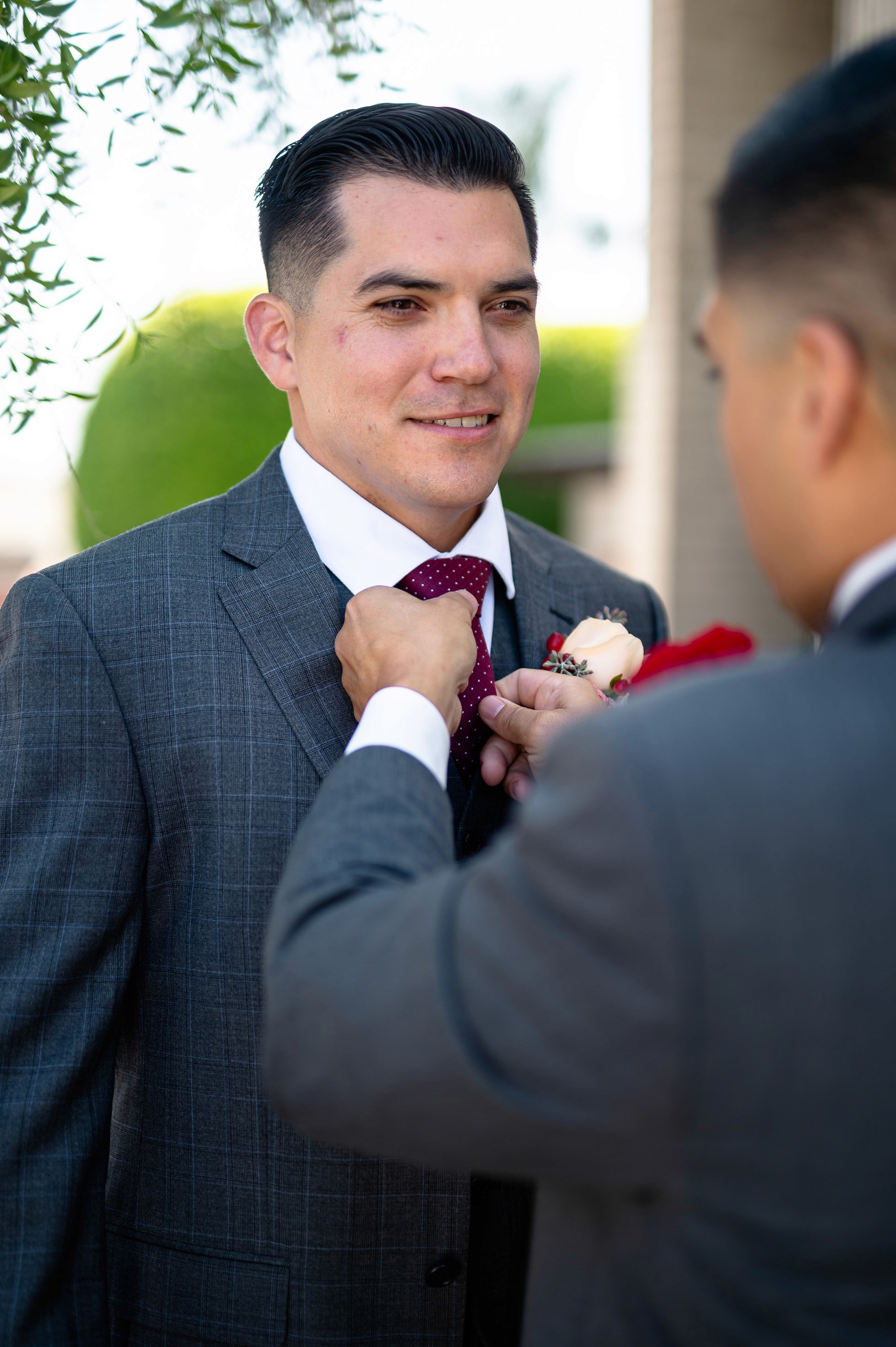 Best man helping groom with boutonniere and tie outside church