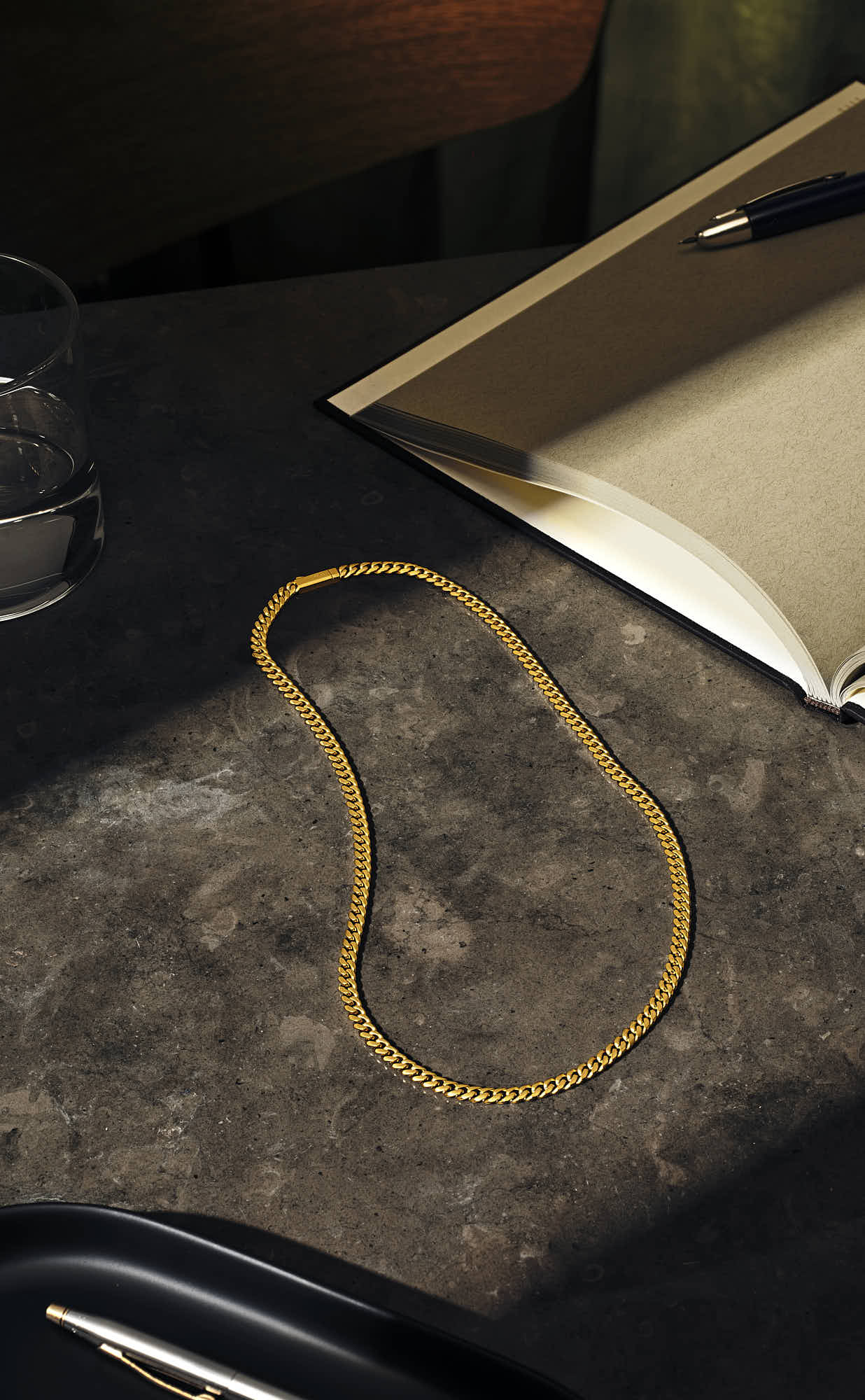 Elegant gold chain necklace on a dark stone surface with an open notebook and pen.