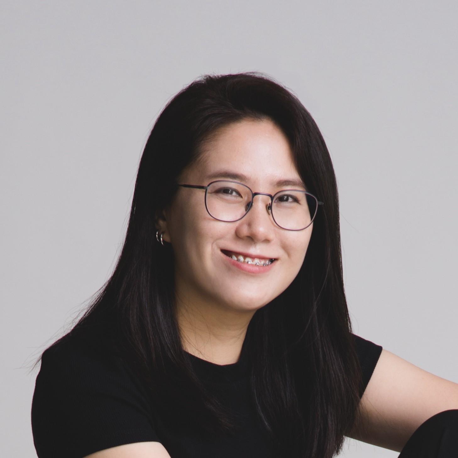 A person wearing headphones sits at a desk with a large curved monitor displaying graphic design software, surrounded by a laptop, smartphone, and potted plant, creating a modern workspace setup.