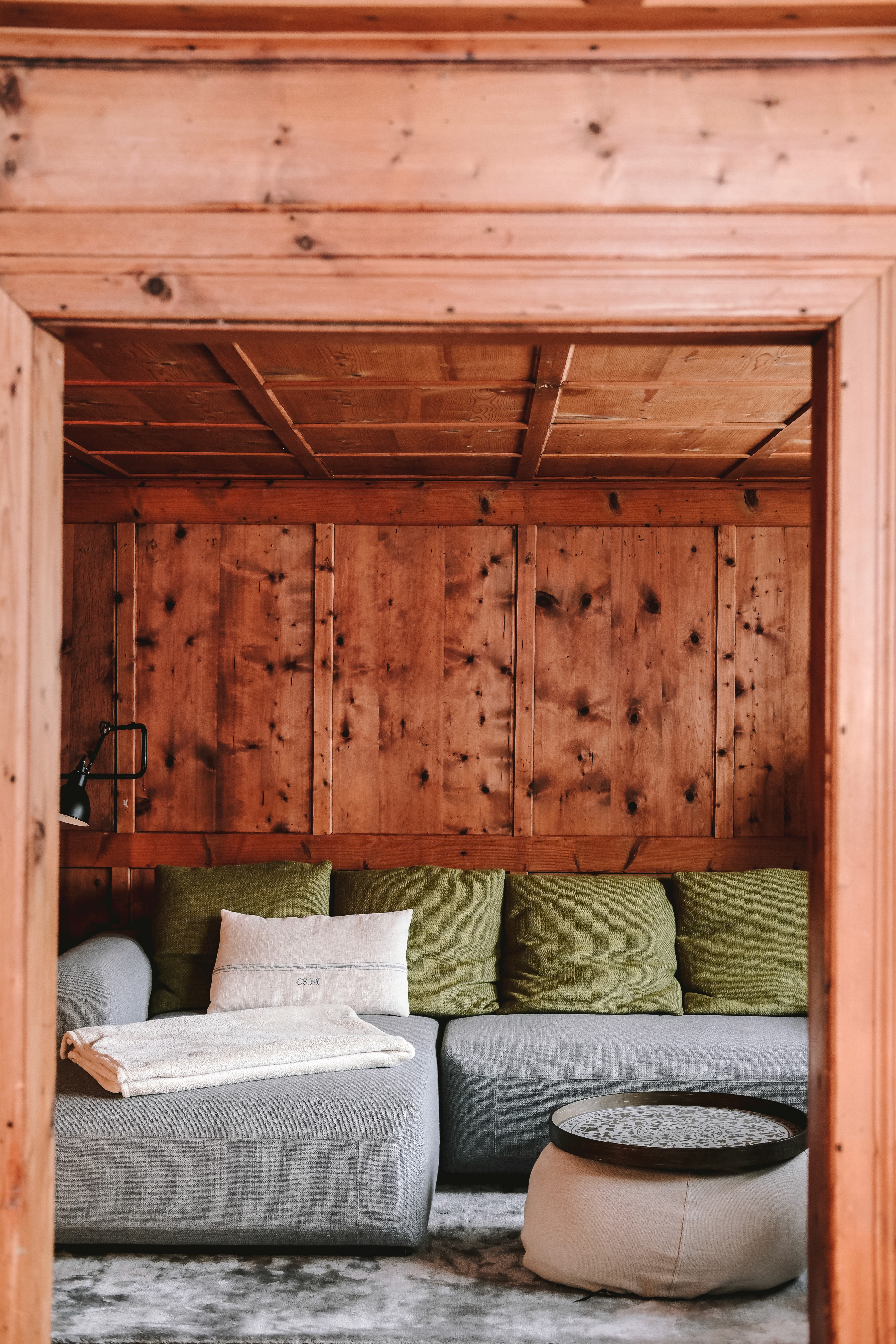 A greay sofa with green pillows in the wooden living room of Benedikta Montafonerhaus