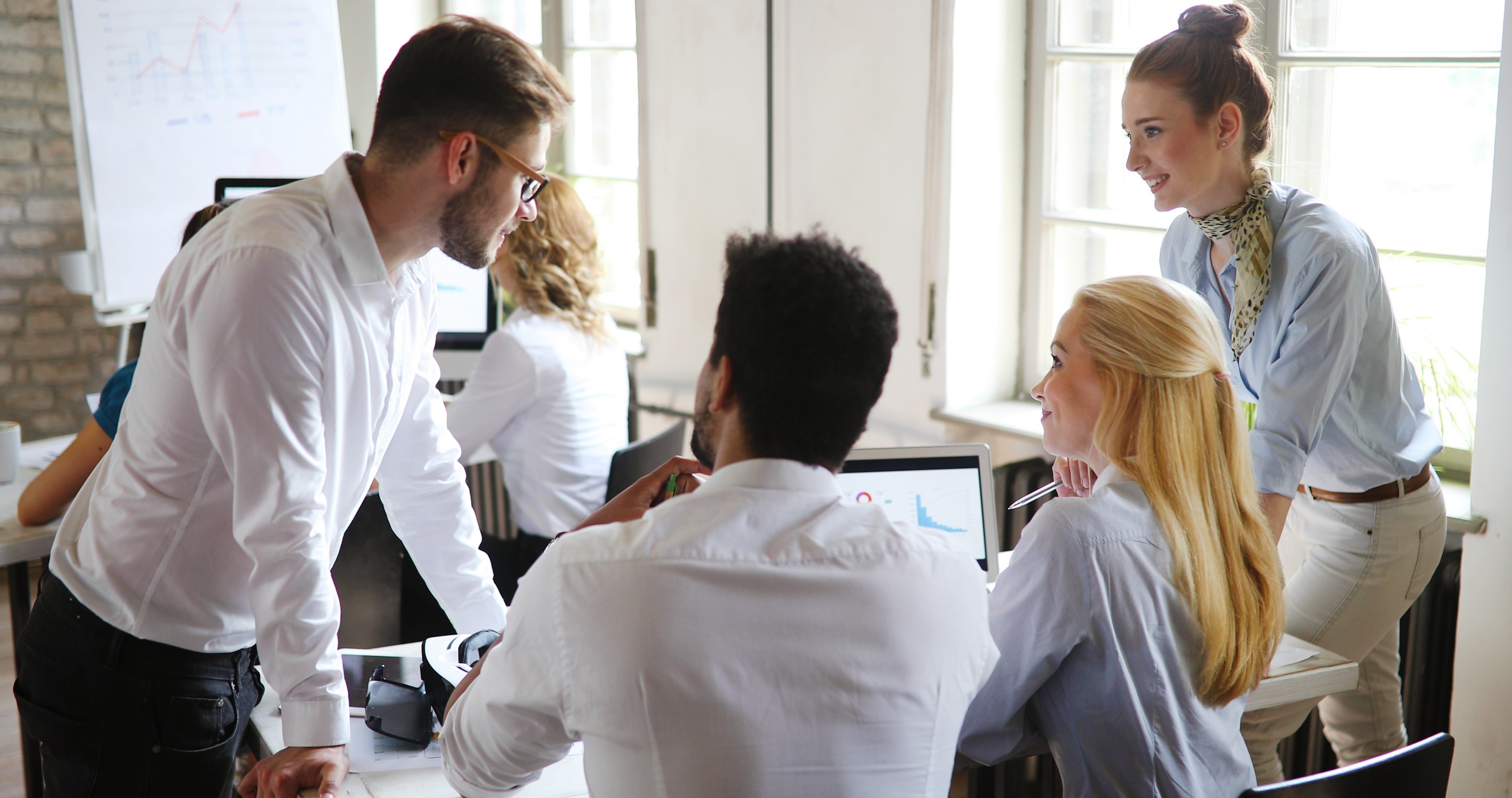 Team collaborating around performance data on laptops, representing a shared marketing dashboard used to align decisions and drive commercial outcomes.