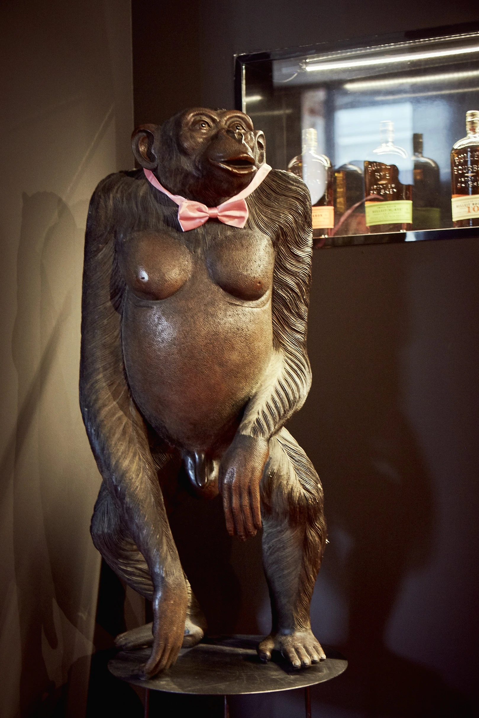 Carved monkey sculpture with a pink bow tie next to an illuminated whisky shelf at DIAGEO BCB17.