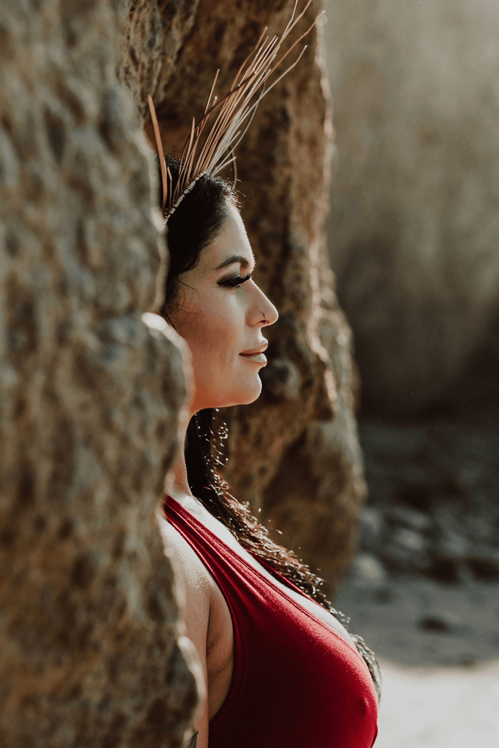 “Gayle Fuller standing between coastal rocks in a red dress, gazing ahead in deep reflection, representing inner alignment and sacred feminine energy”