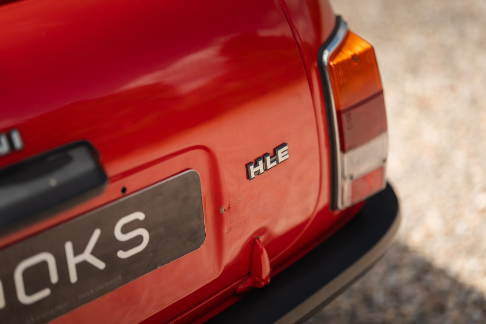 Close-up of a red car's rear, showcasing the bumper and part of the brand name on the license plate.