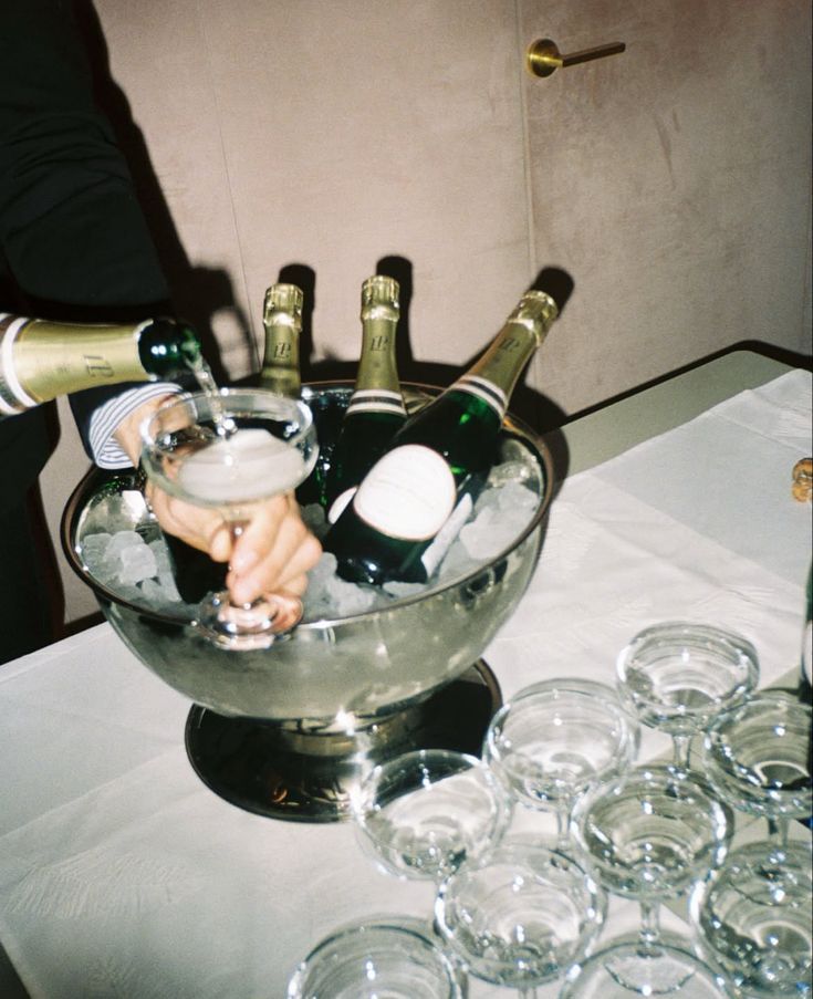Someone pouring champagne into coupe glasses from an ice-filled bucket at a party setup.