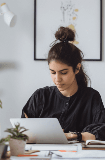 A woman with a bun hairstyle writes on a tablet while sitting at a desk with a minimalist decor.