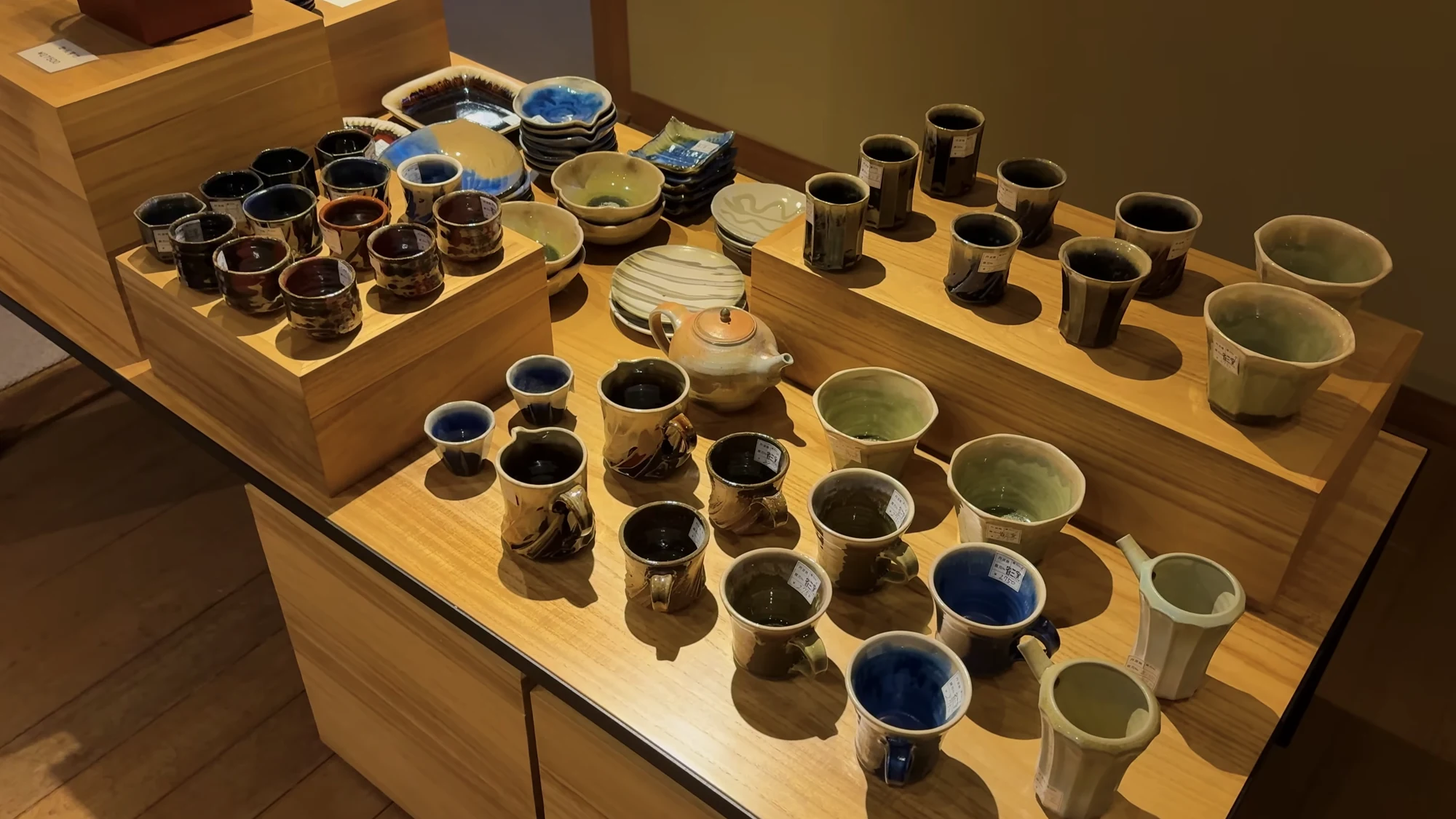 A display of handmade teacups in varied glazes on timber shelves at a Kinosaki inn.