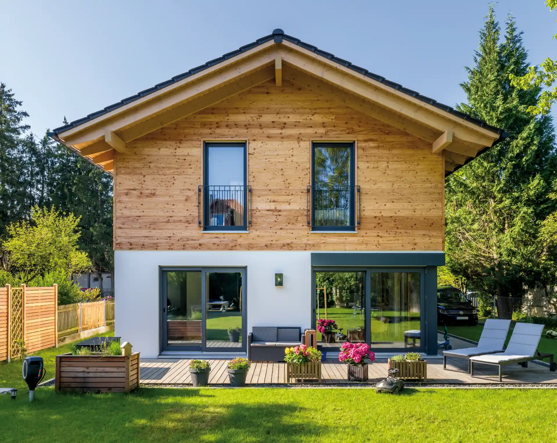 Holzhaus mit Solaranlage auf dem Dach, überdachter Veranda mit Glasdach und Terrassenmöbeln, umgeben von grünen Bäumen.