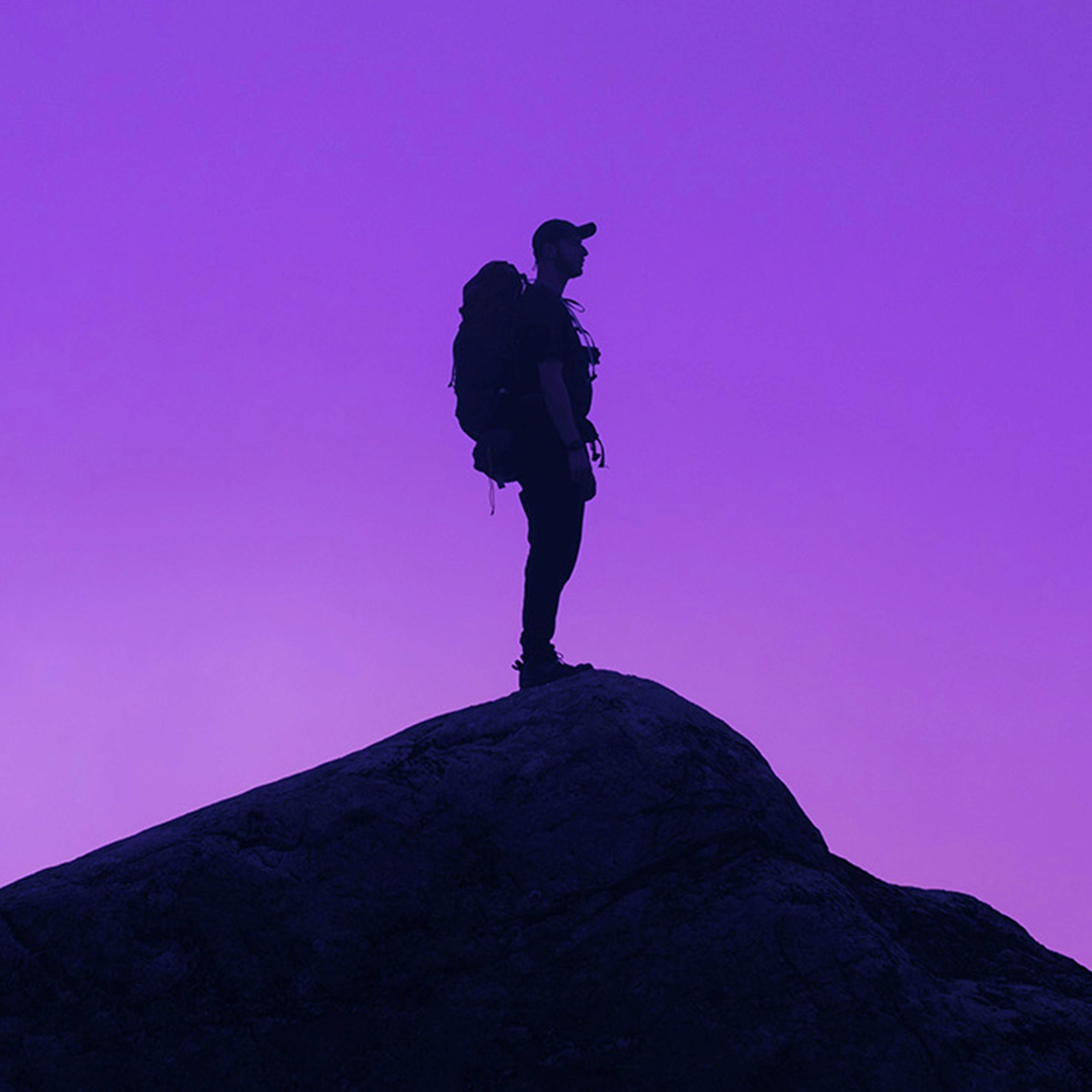 A backpacker on top of a hill with a purple sunset.