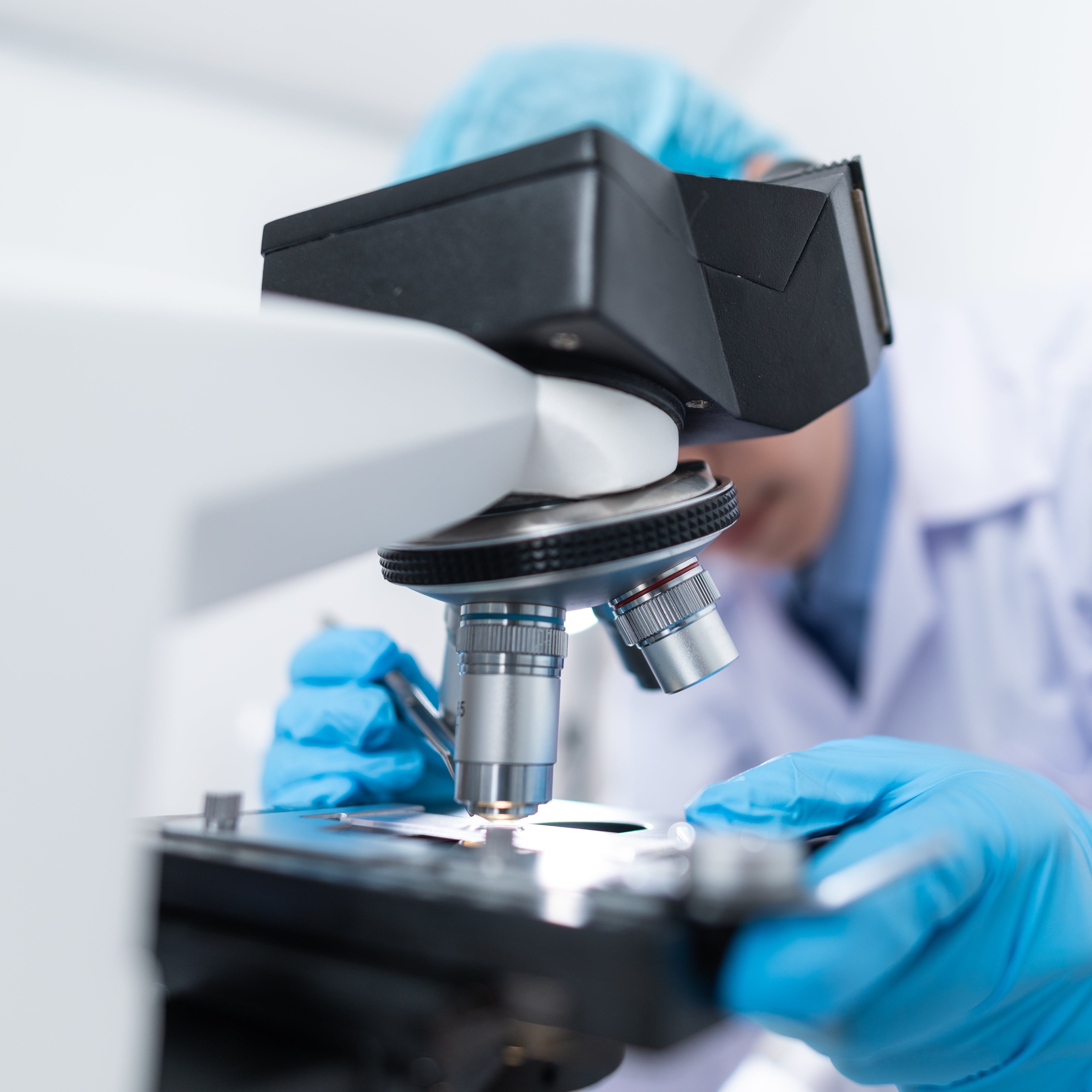 Close-up of a researcher adjusting a microscope in a laboratory setting, highlighting the precision and technical skill required in scientific examination and analysis.