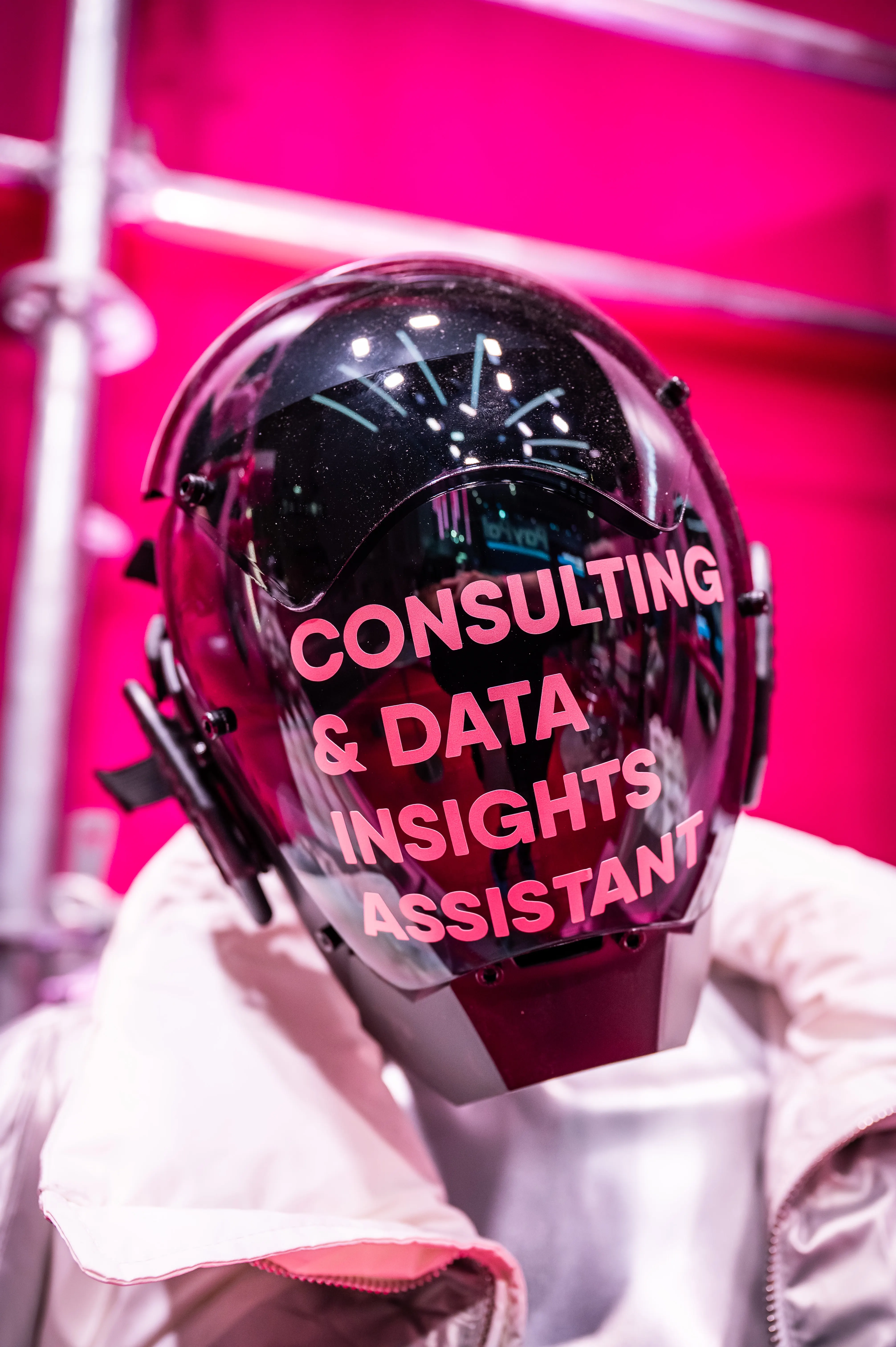 Figure in silver suit with black helmet reading Consulting & Data Insights Assistant in front of the pink booth wall.