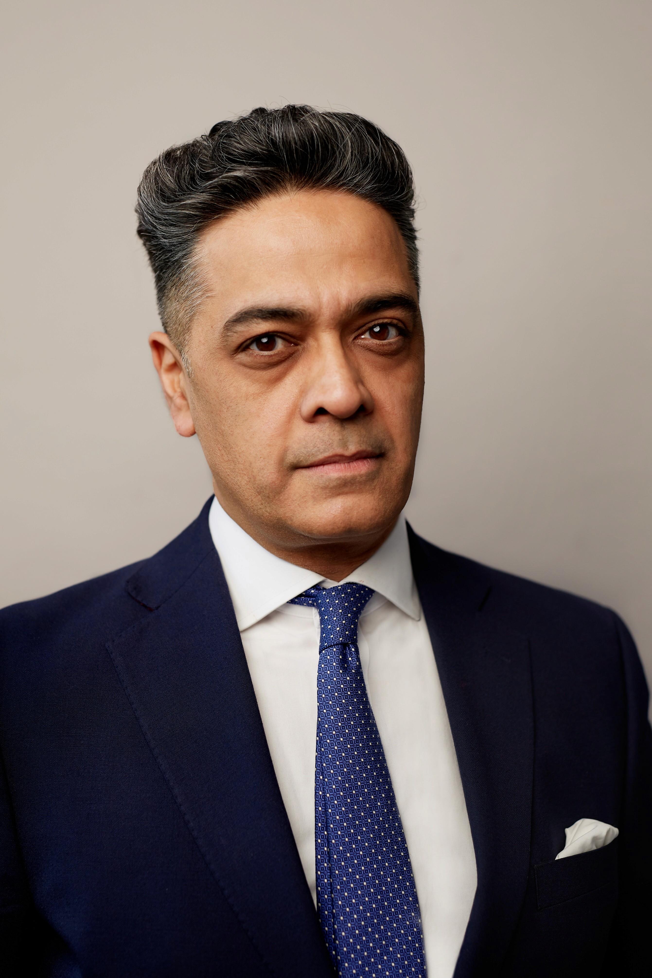 Man in a navy suit, white shirt, and patterned blue tie.
