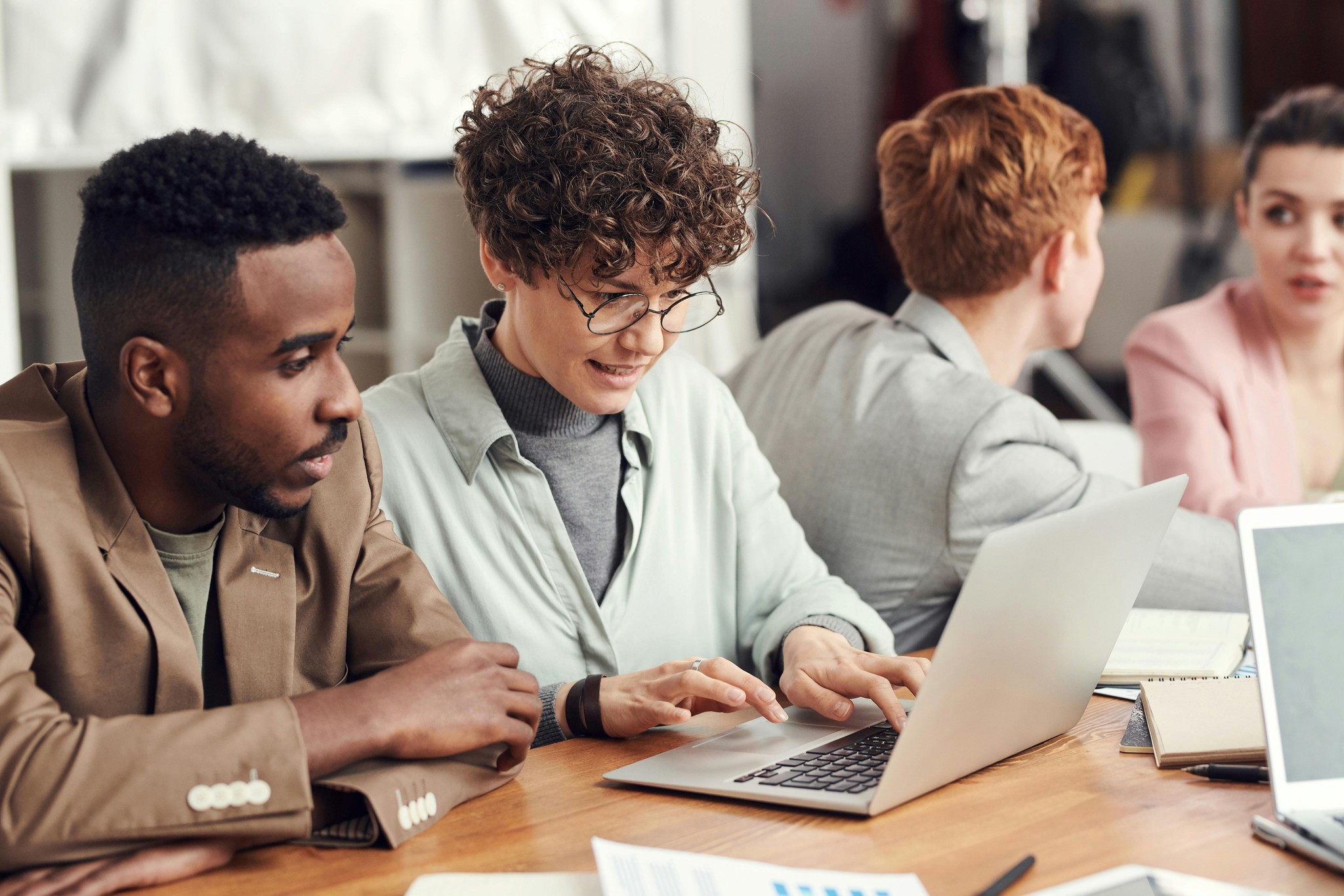The image depicts several colleagues collaborating on a laptop, suggesting teamwork, brainstorming, or a professional discussion in an office setting.