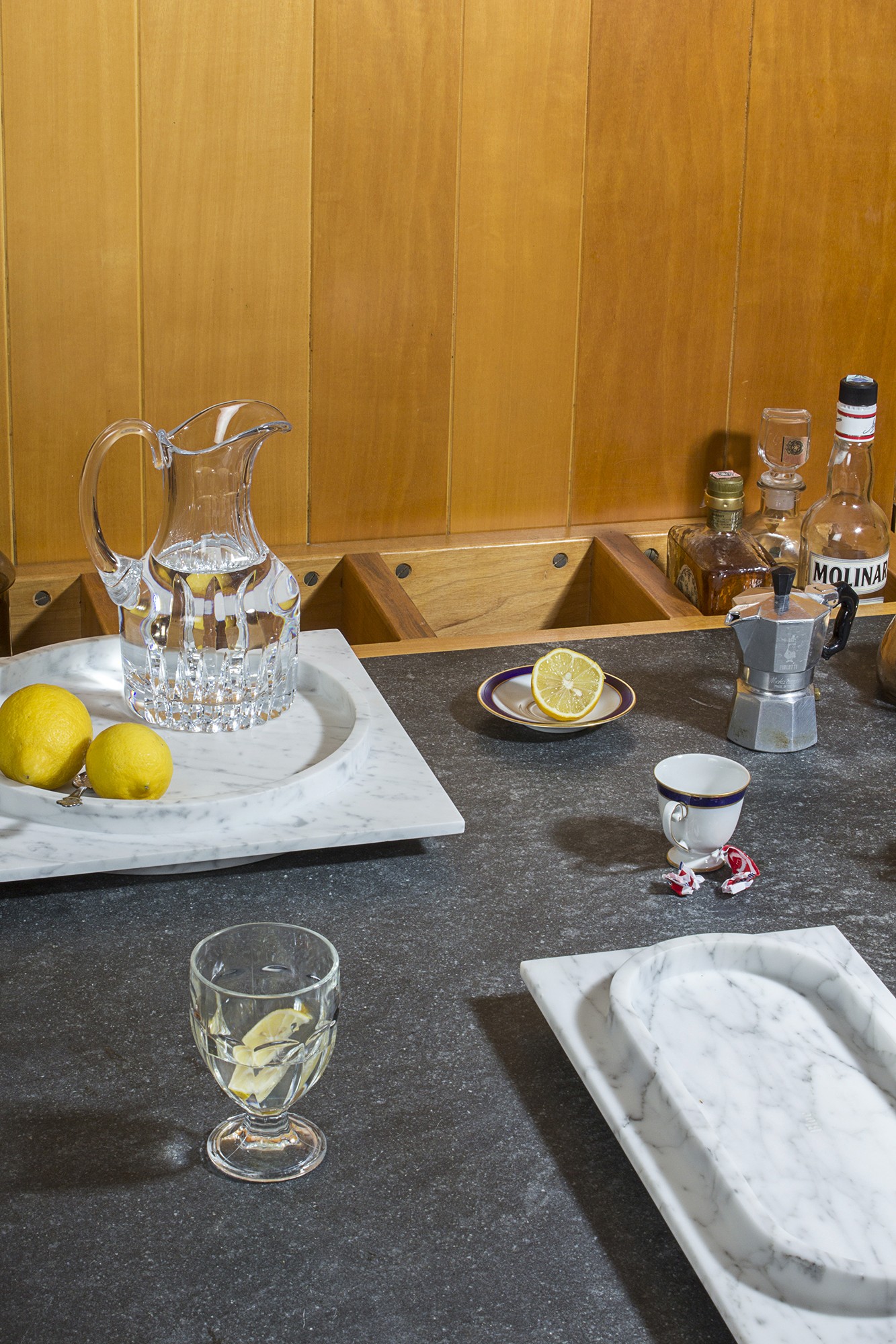 Photo d'une table de cuisine à l'ancienne sur laquelle est posée un plateau en marbre et dans lequel sont posés une carafe d'eau pleine et des citrons