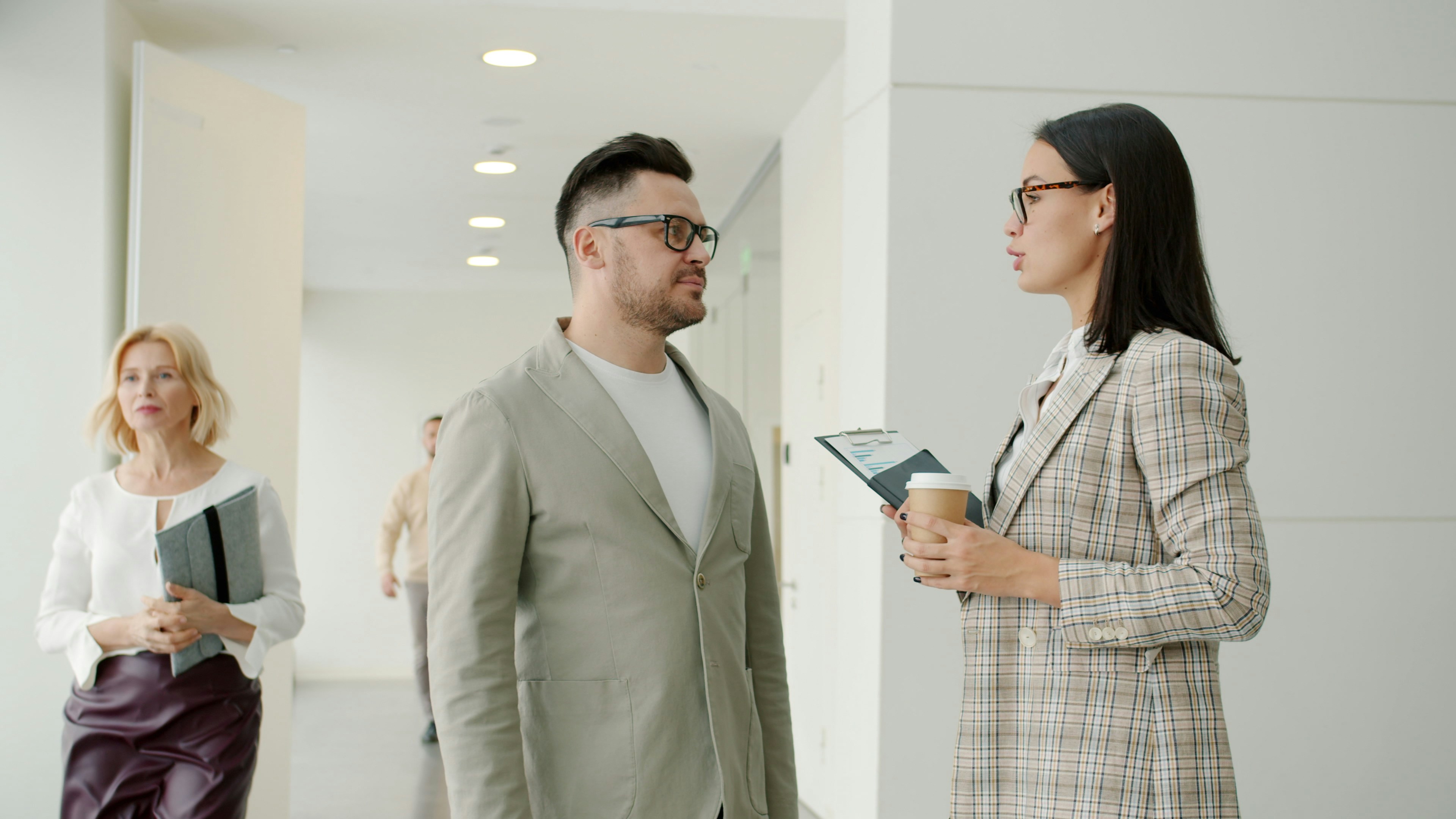 Two colleagues talking in a modern office hallway.