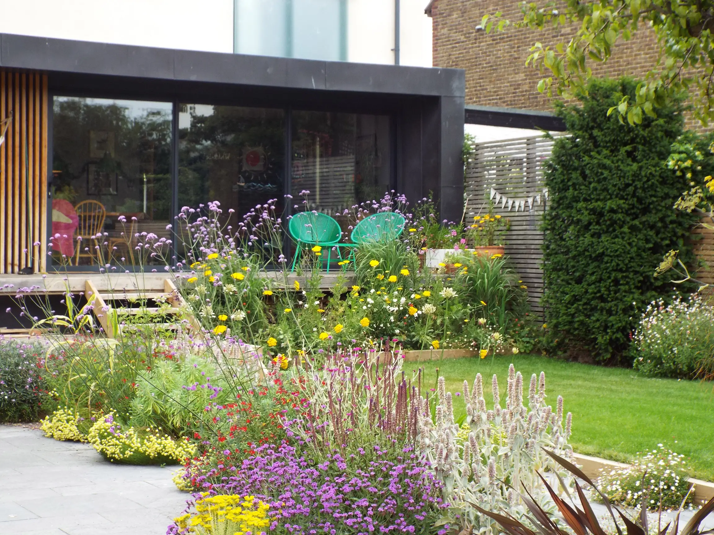 A modern building with large windows, surrounded by a colorful garden featuring various plants and greenery.