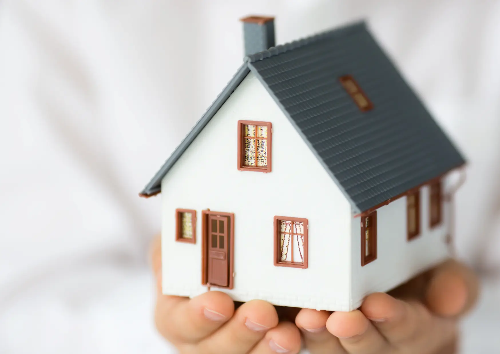 Hausmodell in Händen als Symbol für Auftrag mit Wohngarantie beim Immobilienverkauf