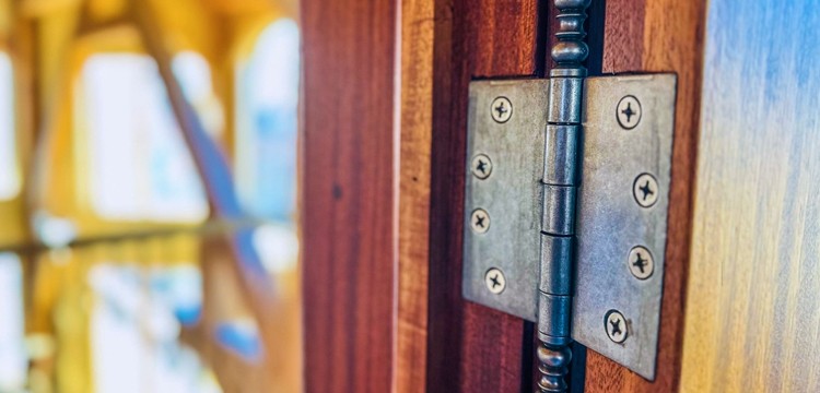 Close-up of antique dark hinges on a wooden door, highlighted by the sunny ambiance.