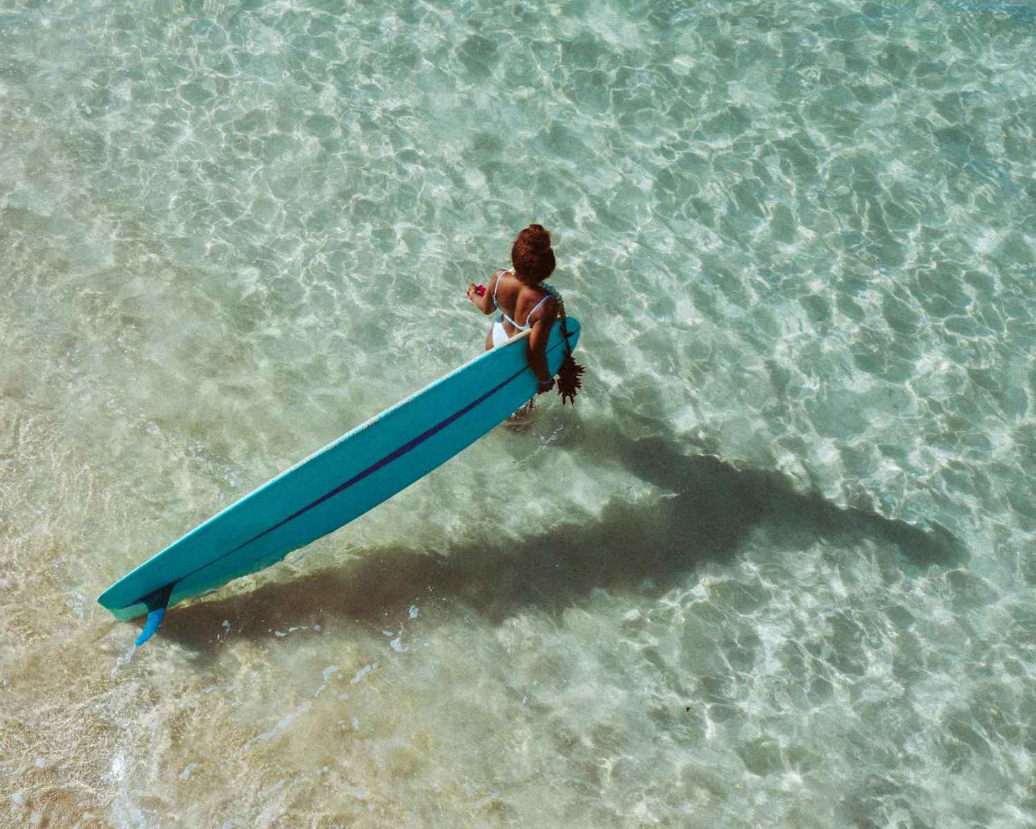 Bird's-eye view of a surfer on a longboard in crystal clear water — surfboard rental in Caribbean