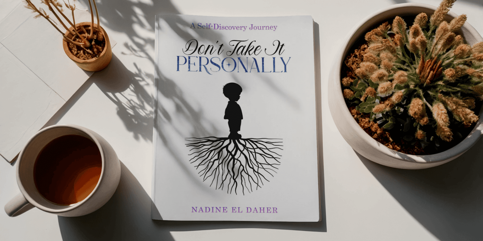 A book titled "Don't Take It Personally" by Nadine El Daher placed on a table with plants and a cup.