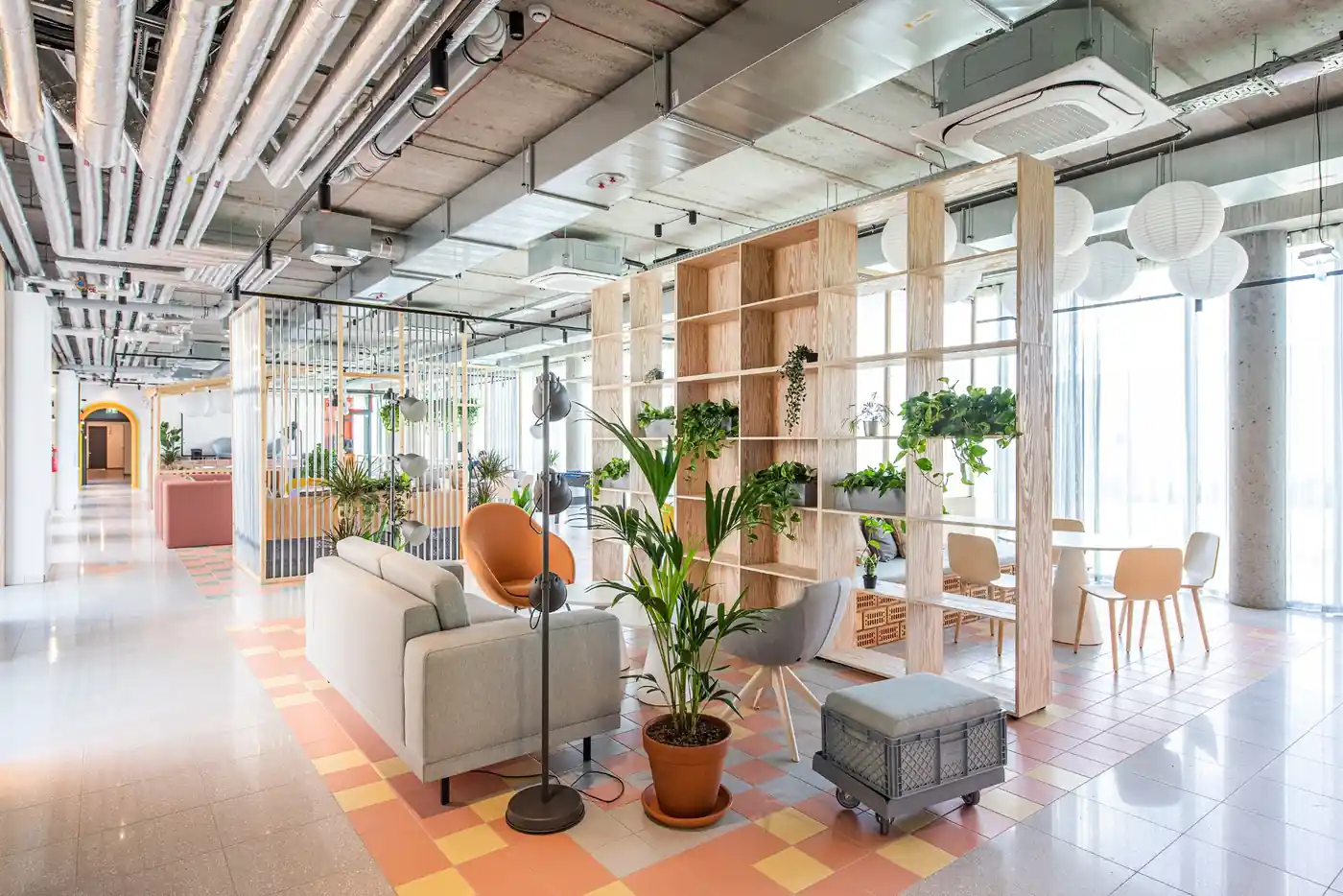 Bright shared lounge in Vilnius student accommodation with seating, tables, plants and natural light.
