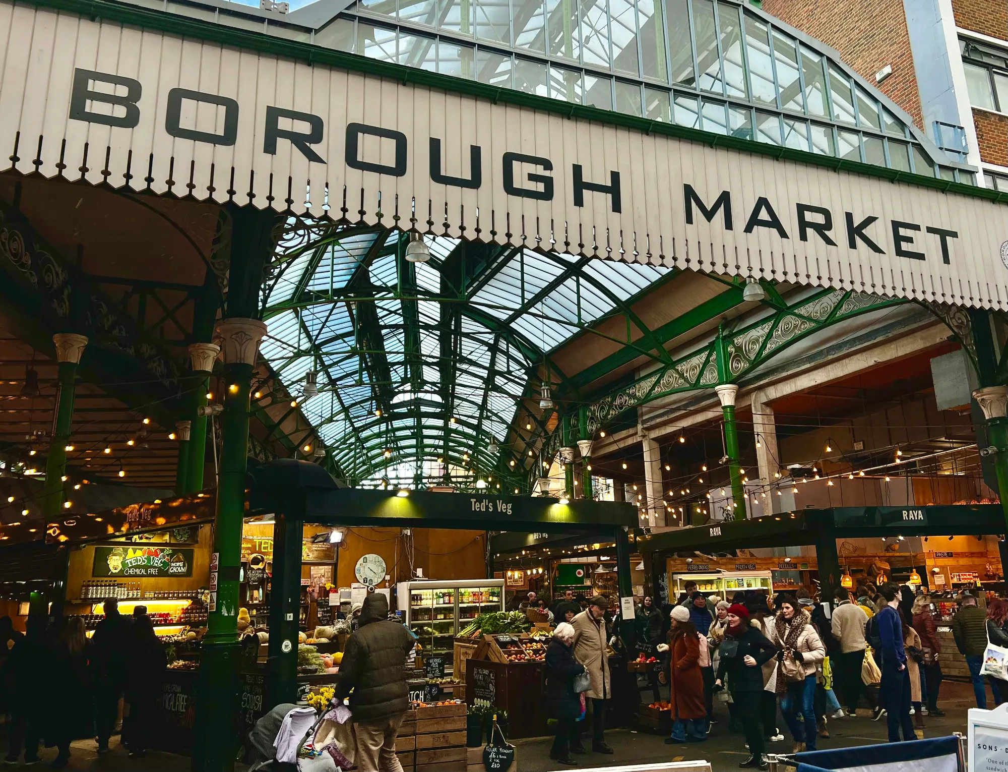 Borough Market entrance sign with people shopping under a glass and metal roof structure.