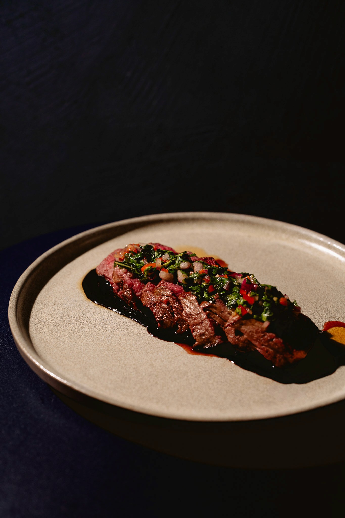 Person with a mustache wearing a black t-shirt carrying a tall stack of pizza boxes inside a dimly lit bar or restaurant.