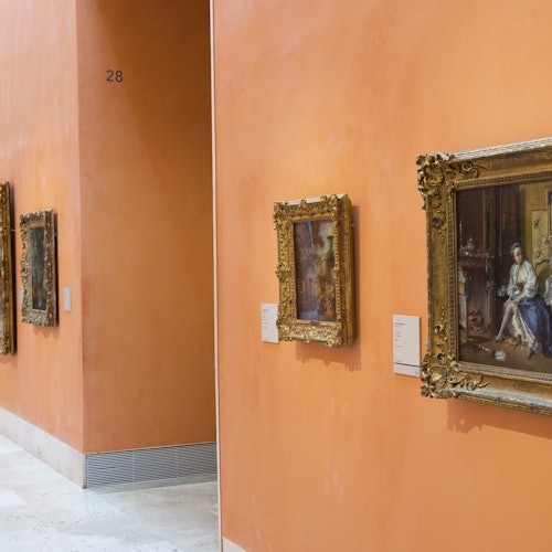 Galeria sztuki z pomarańczowymi ścianami, na których wiszą oprawione obrazy. Etykiety obrazów są widoczne obok każdego dzieła sztuki. Ściana oznaczona cyfrą "28."