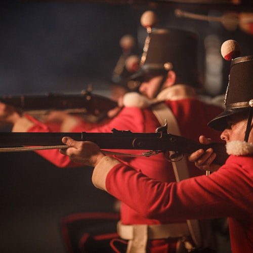 在一个黑暗烟雾弥漫的环境中，身穿红白相间制服的士兵们目标明确，头戴黑帽，上面装饰着白红相间的绒球。