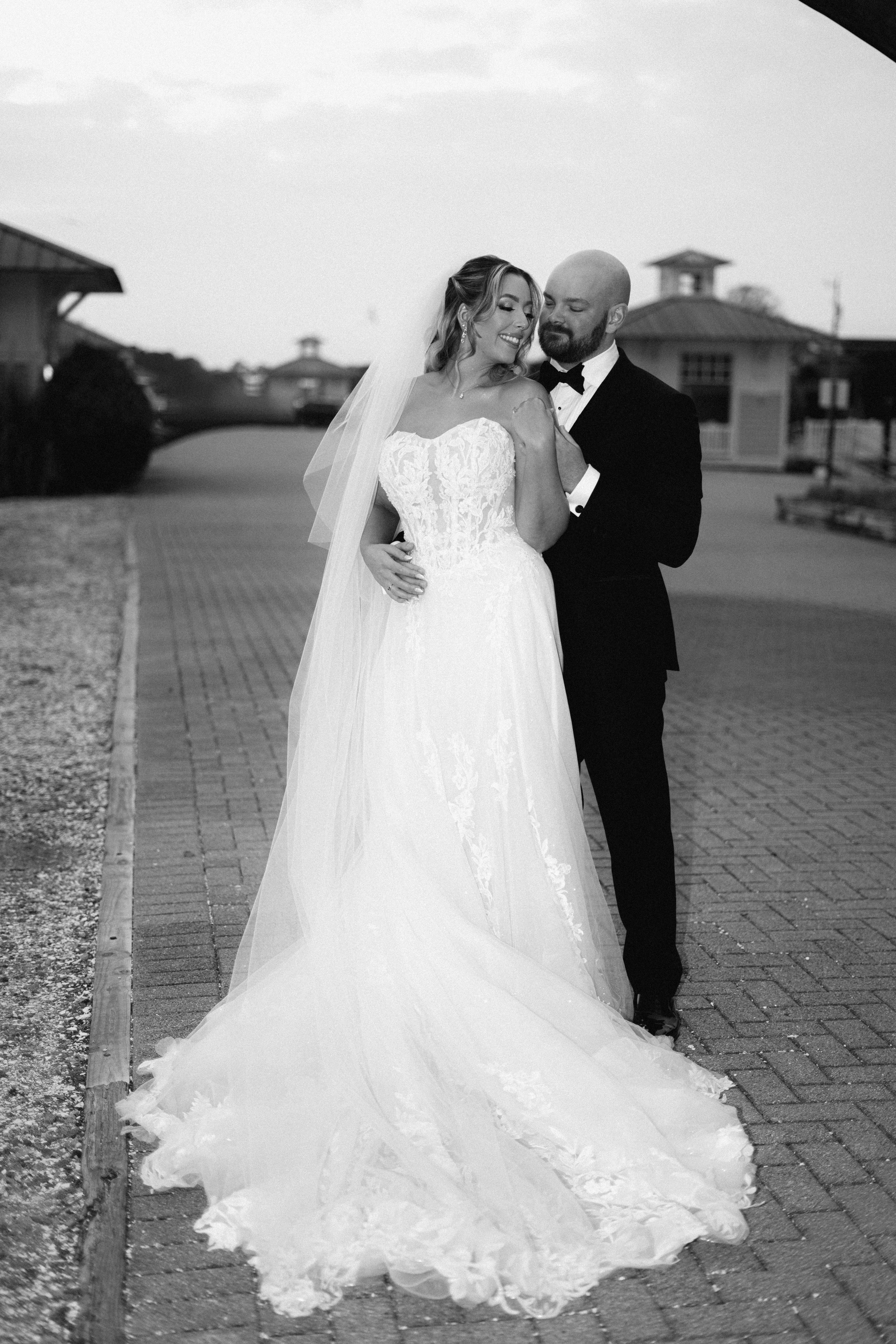 A couple in wedding attire walks hand in hand across a sunlit field.
