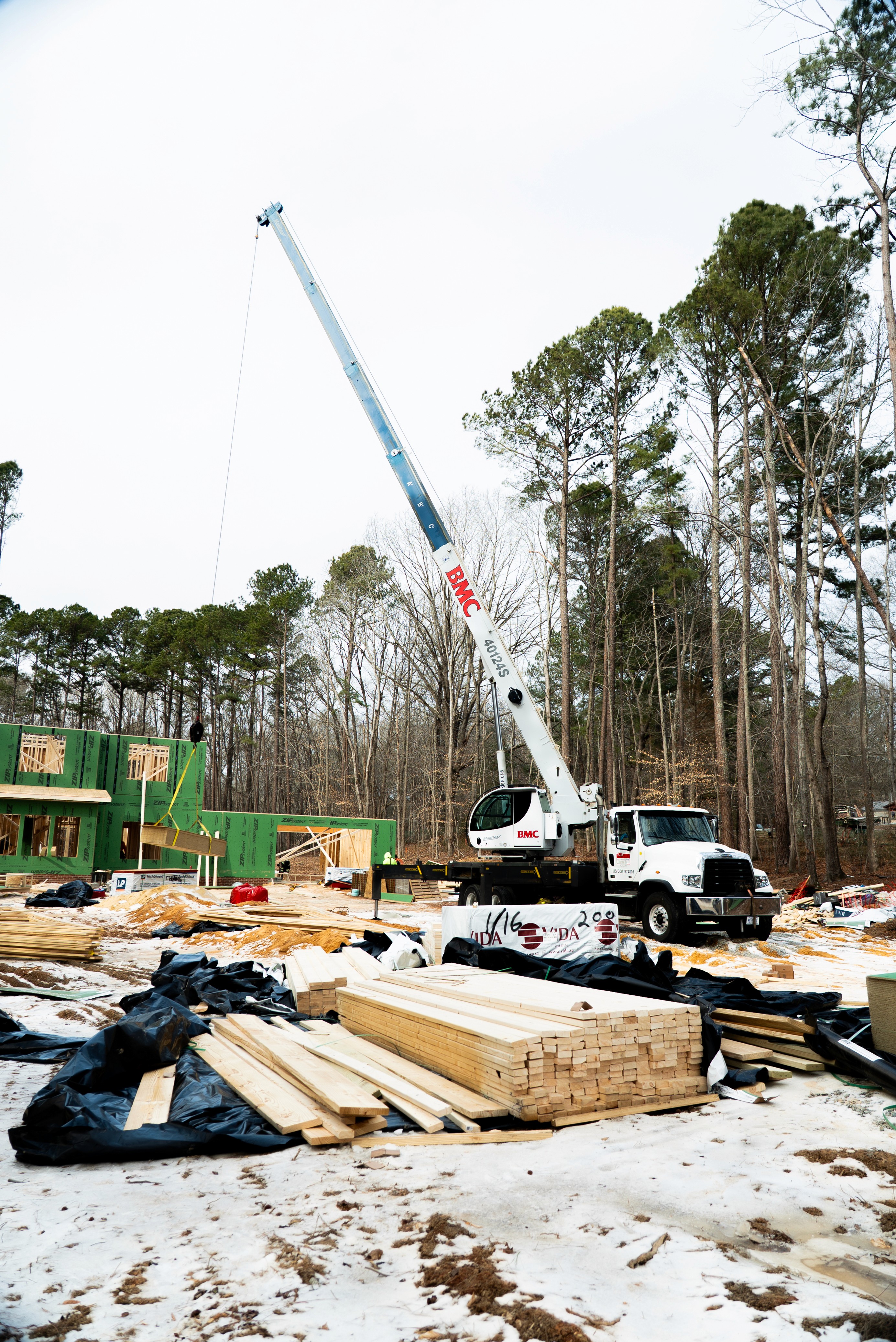 BMC crane lifting trusses on a commercial construction site with lumber stacks in foreground